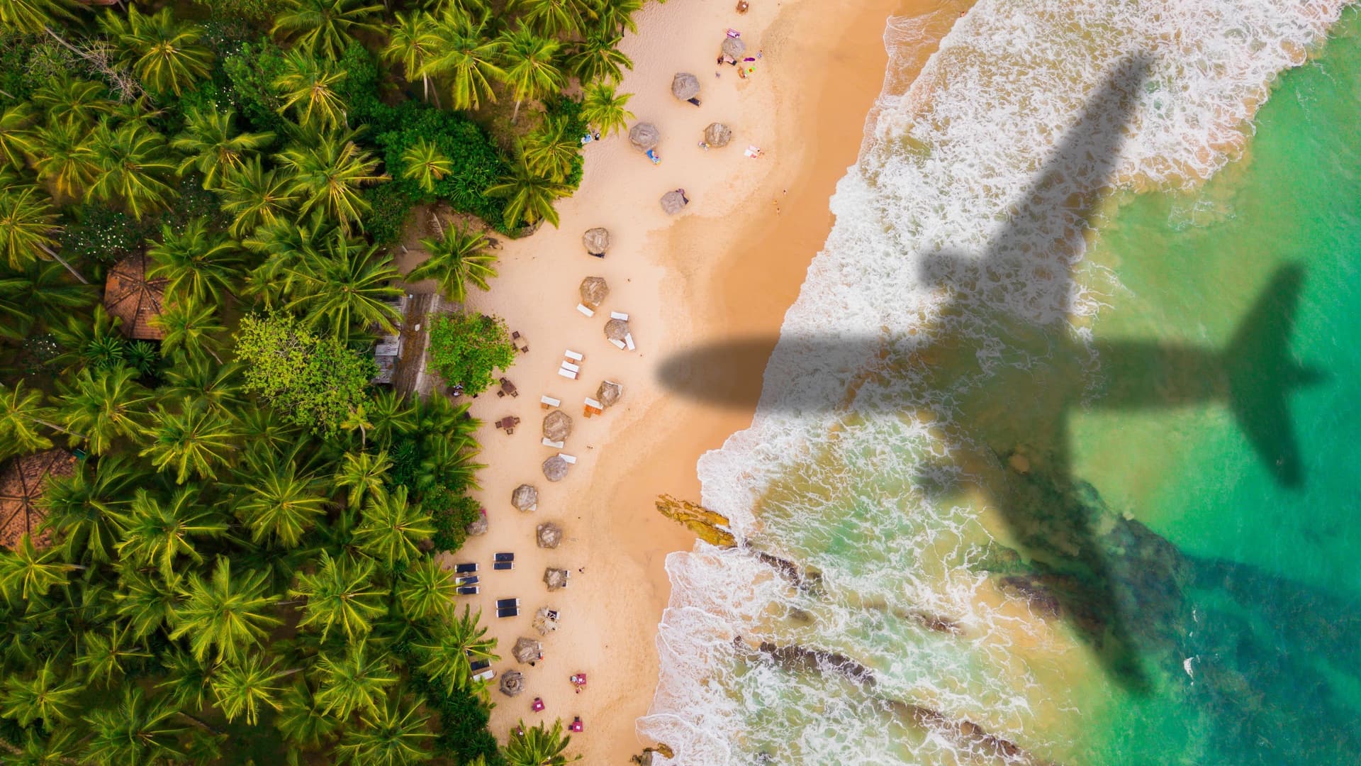 Ein Flugzeug fliegt über einen karibischen Strand. Man sieht nur den Schatten des Flugzeugs auf dem Strand.