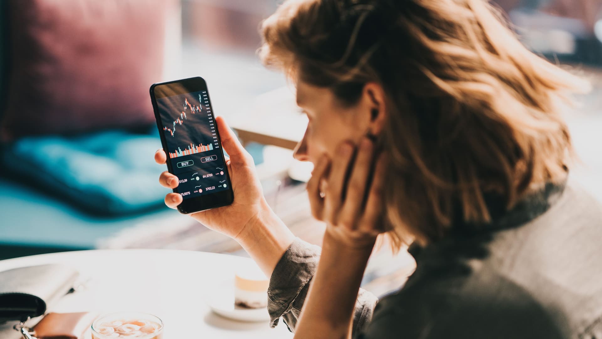 Frau sitzt im Café und schaut sich ihr Börseninvestment auf ihr Handy