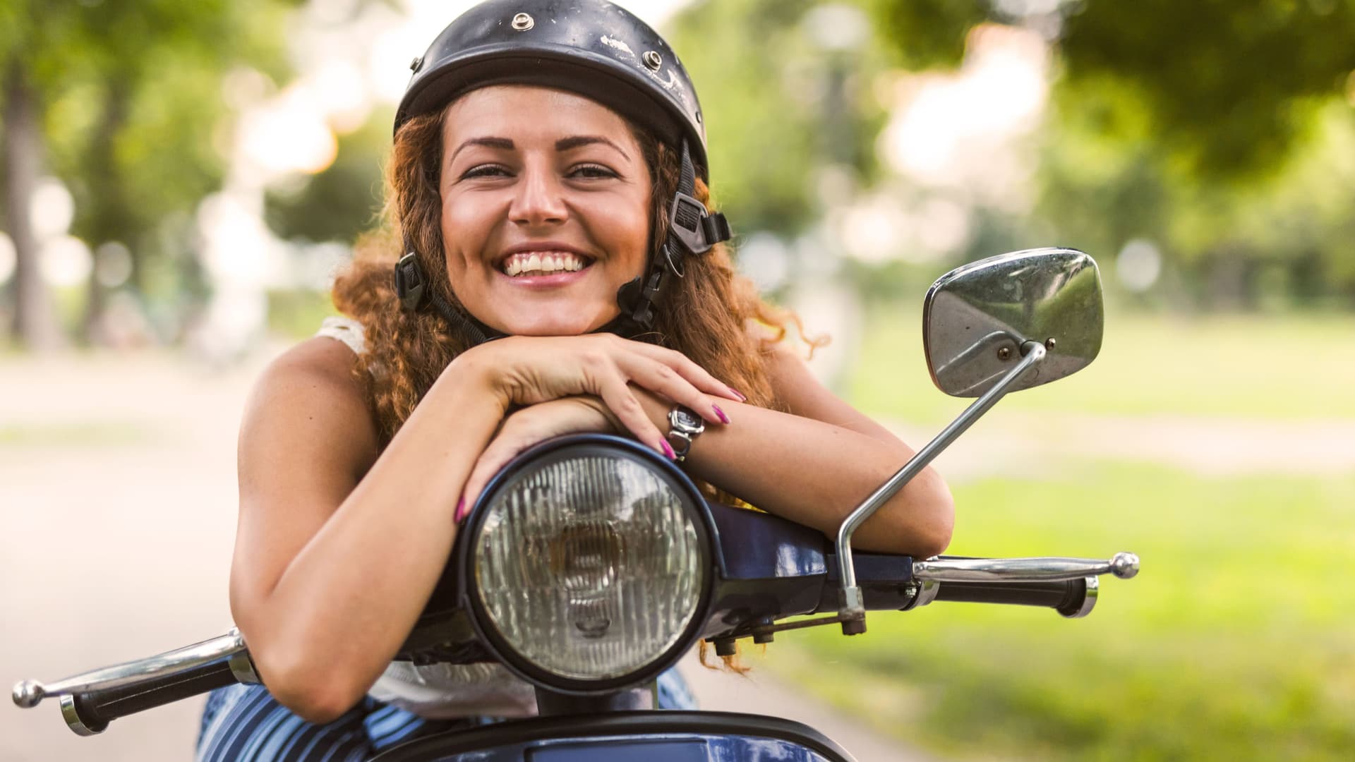 Eine lächelnde junge Frau lehnt auf einem alten Motorrad.