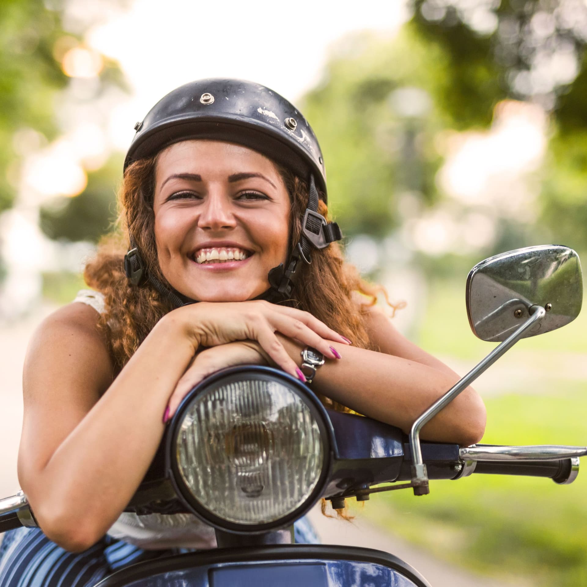 Eine lächelnde junge Frau lehnt auf einem alten Motorrad.