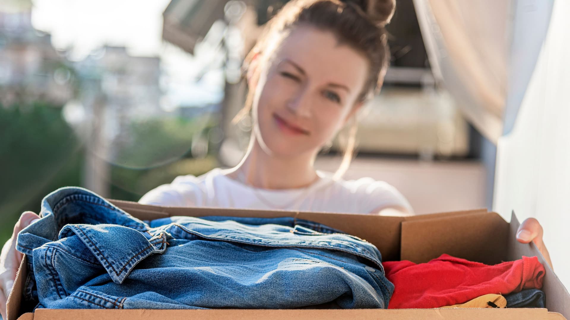Junge Frau hält eine Kiste mit Kleidern in die Kamera