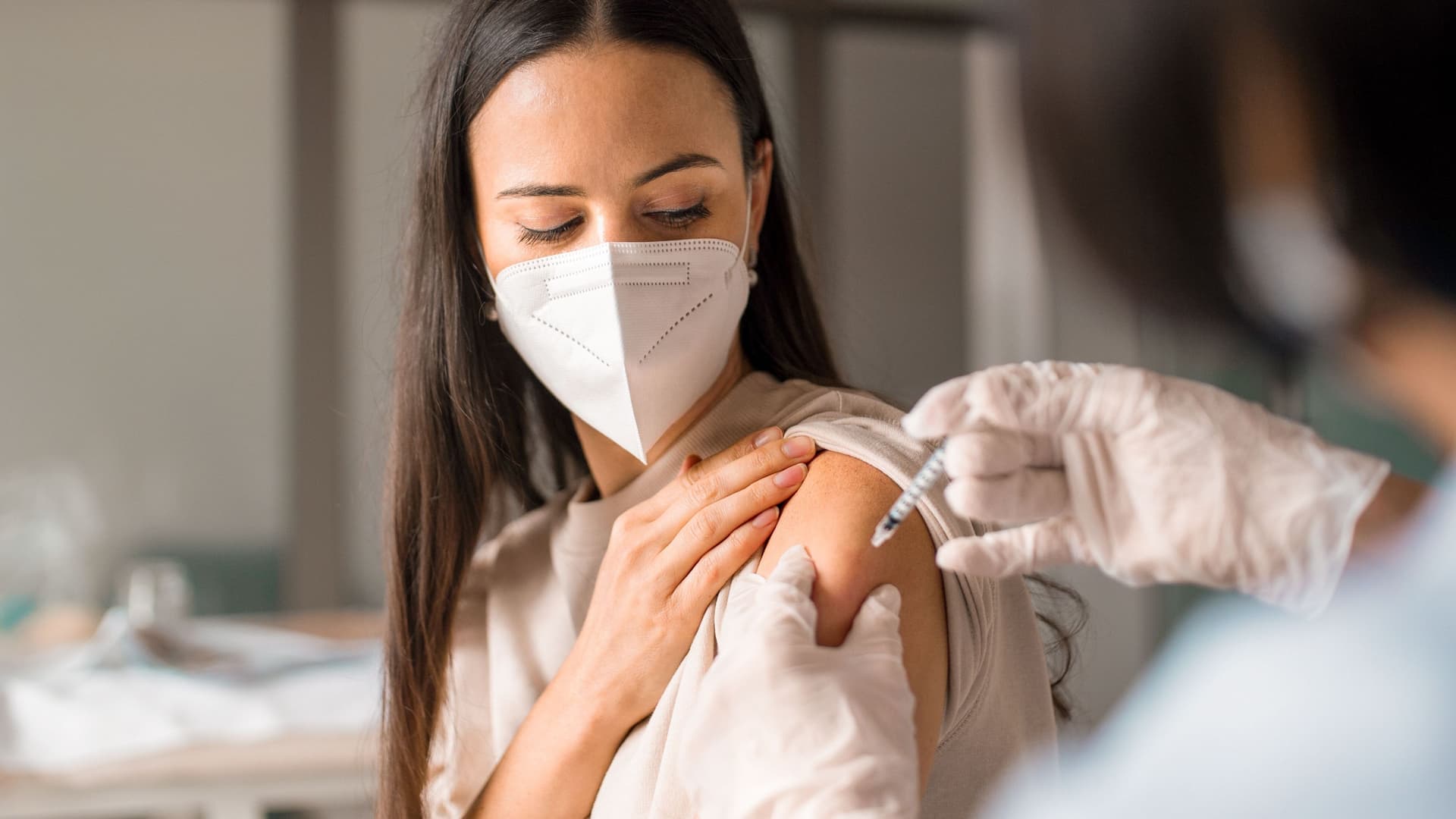 Frau mit Maske bekommt eine Spritze in den Arm