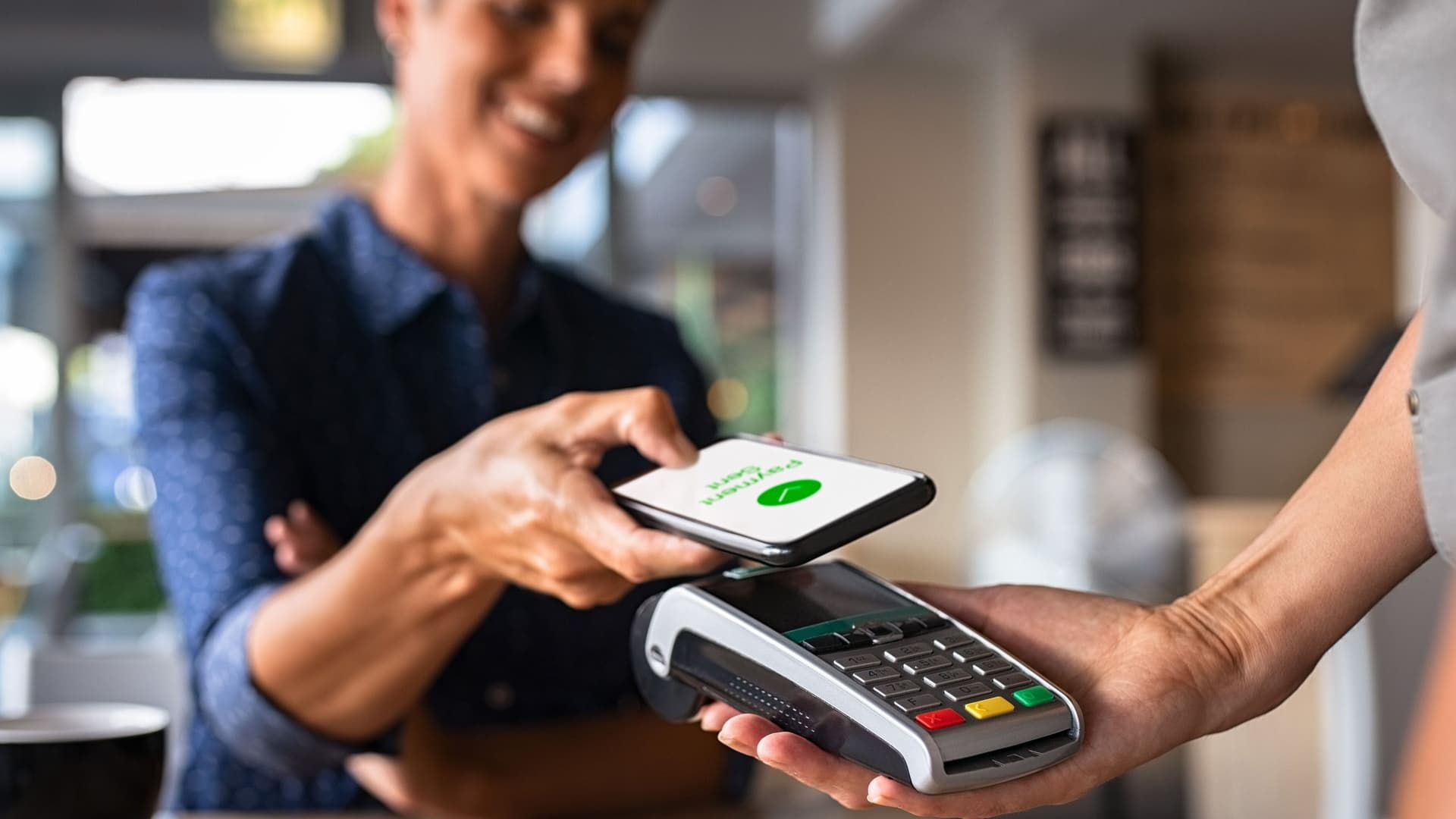Eine Frau bezahlt in einem Café mit ihrem Smartphone. Dabei hält sie ihr Smartphone vor ein Kartenlesegerät.