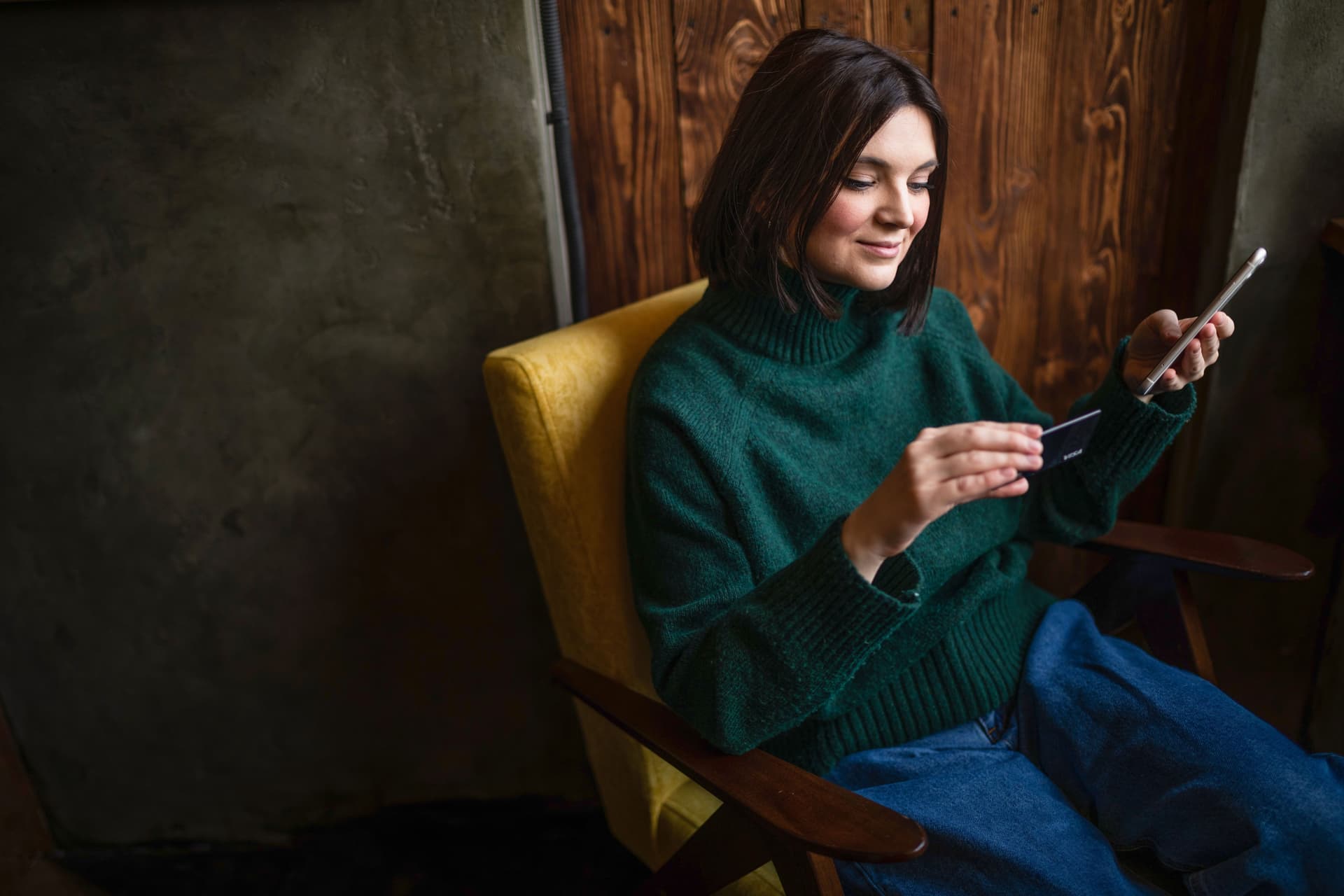 Lächelnde Frau, die online mit einer Kreditkarte und einem Smartphone im Wohnzimmer einkauft.