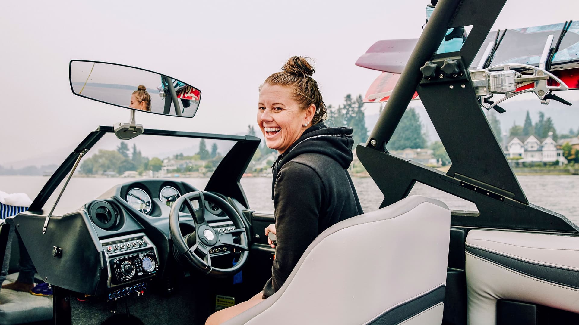 Lachende Frau, die ein Boot fährt, das ein Wakeboard transportiert.