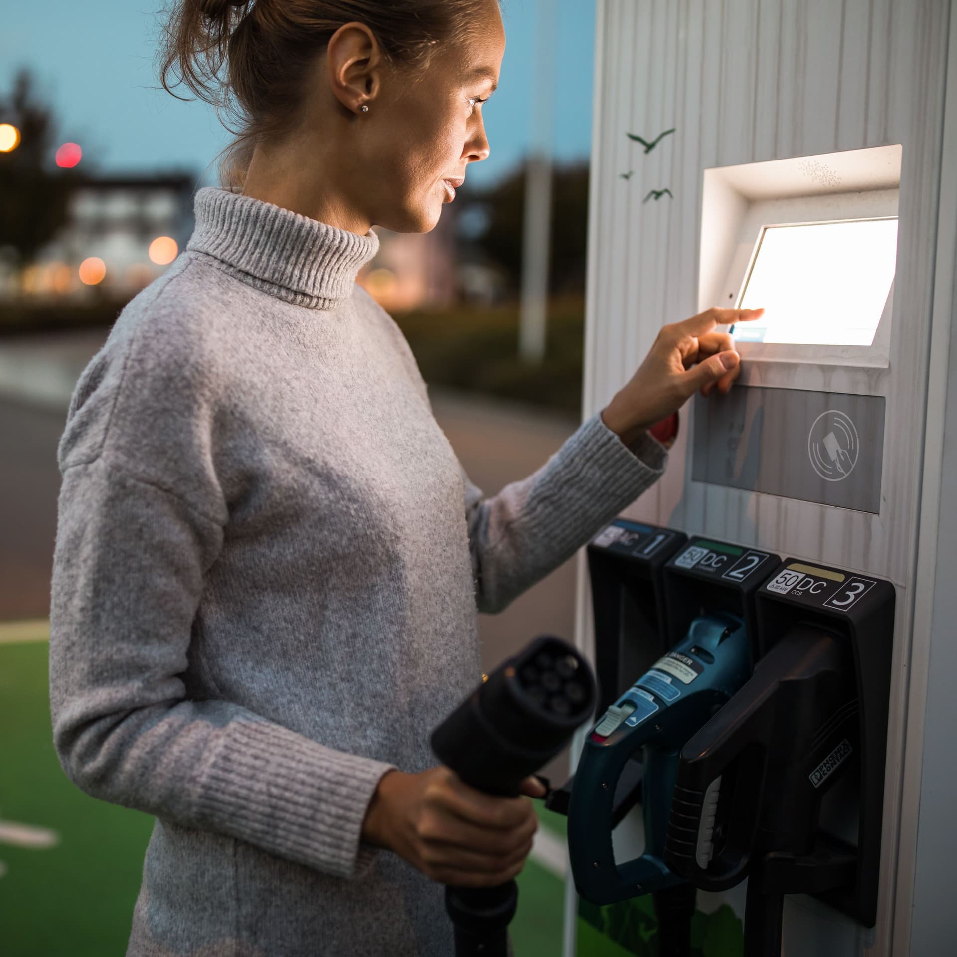 Ein junge Frau bezahlt an einer Ladesäule für Elektroautos.
