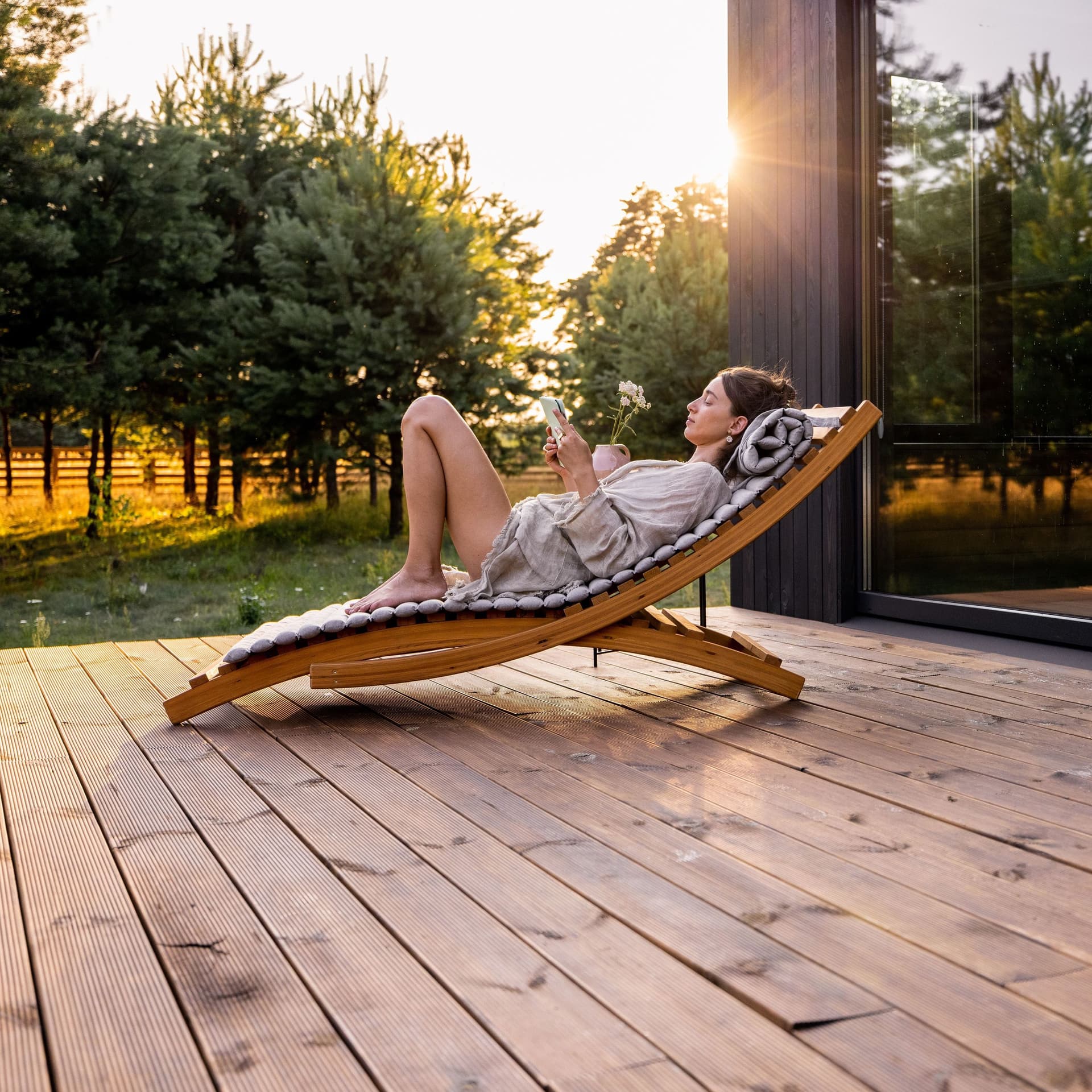 Frau liegt auf einer Sonnenliege auf der Holzterrasse eines Hauses. 
