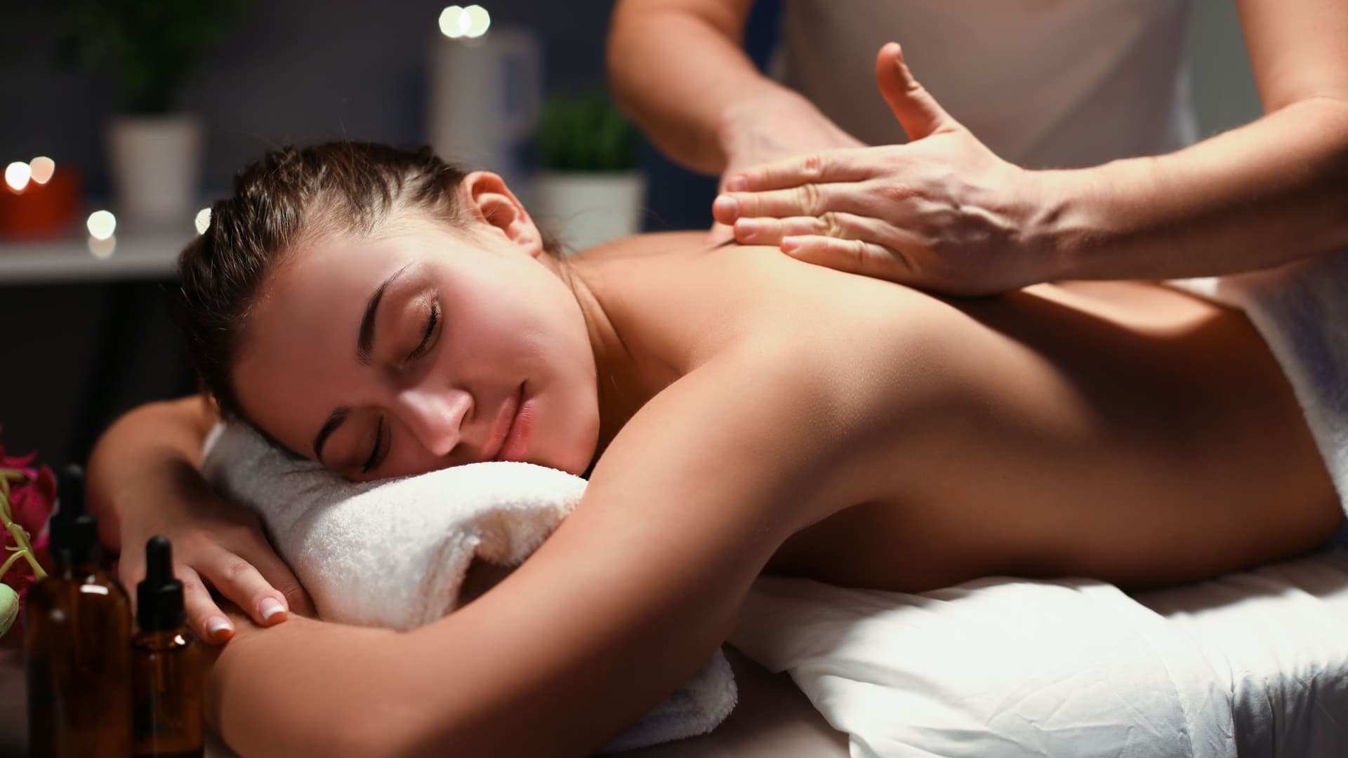 Frau mit geschlossenen Augen auf einer Massageliege, die massiert wird.