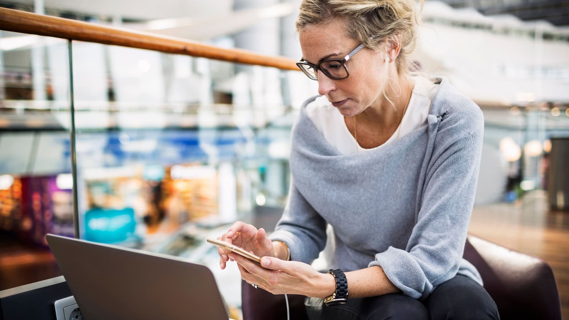 Ein Frau sitzt mit Smartphone und Laptop in einer Flughafenlobby.