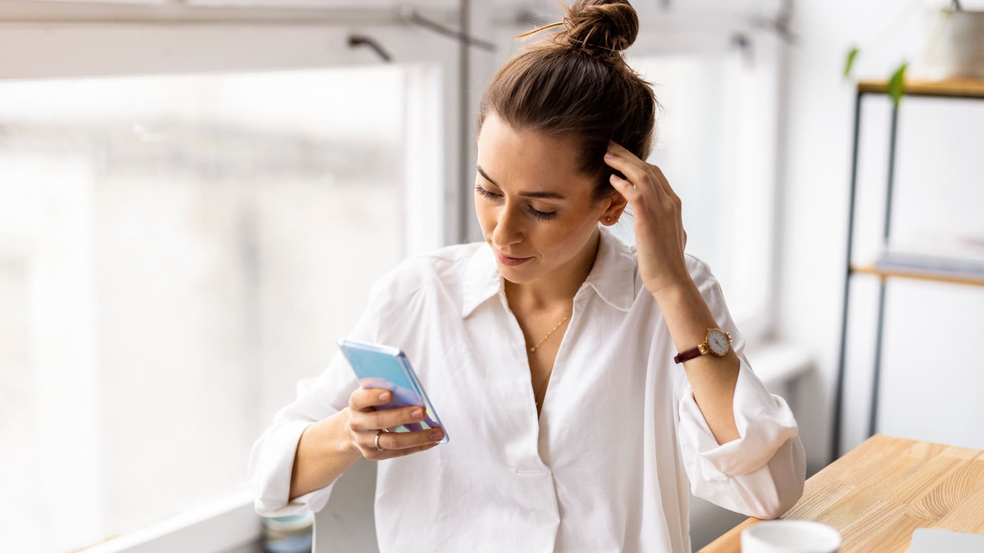 Frau sitzend an einem Tisch mit Tasse, schaut auf ihr Smartphone.