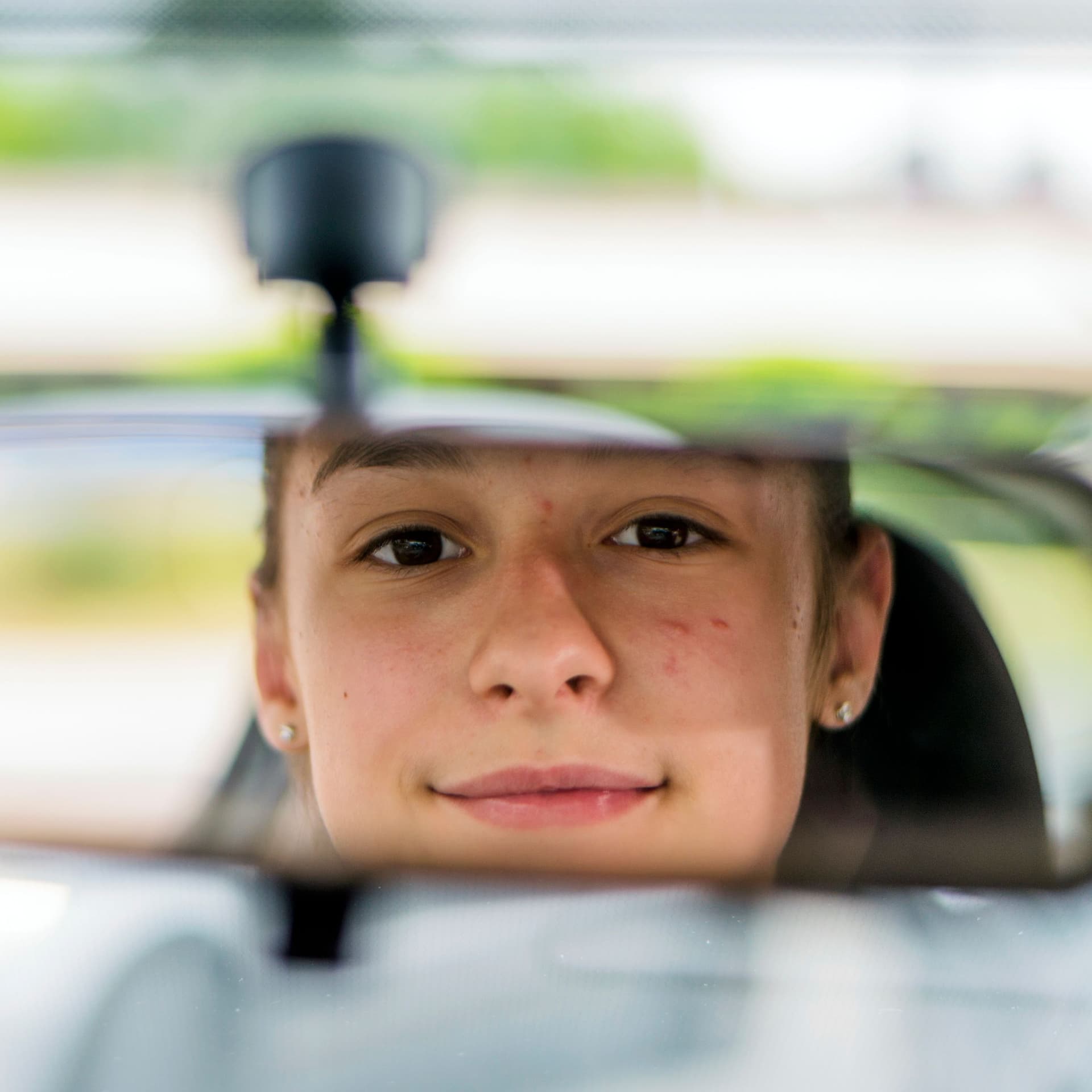Junge Frau schaut im Auto in den Rückspiegel.