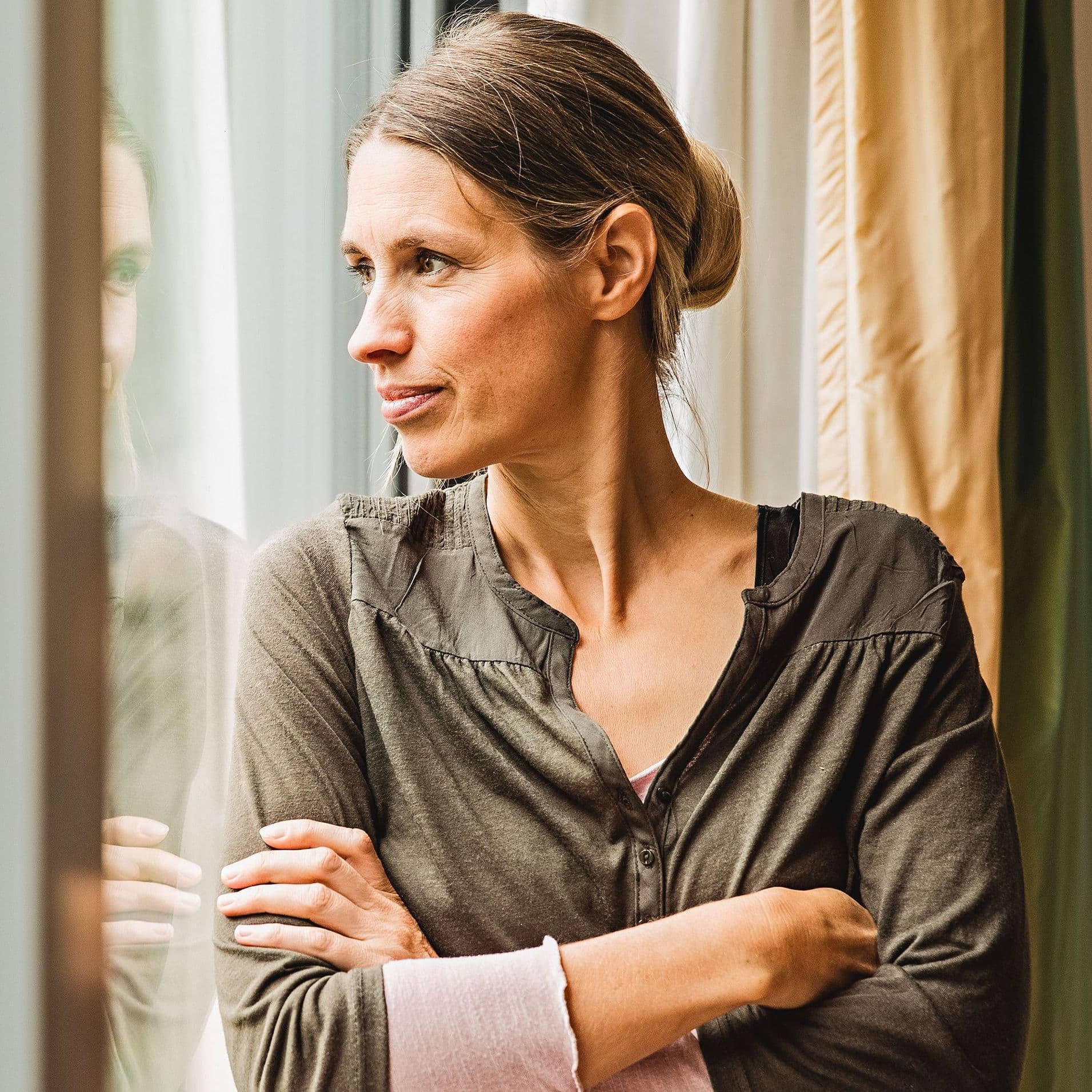 Frau mittleren Alters steht gedankenversunken am Fenster