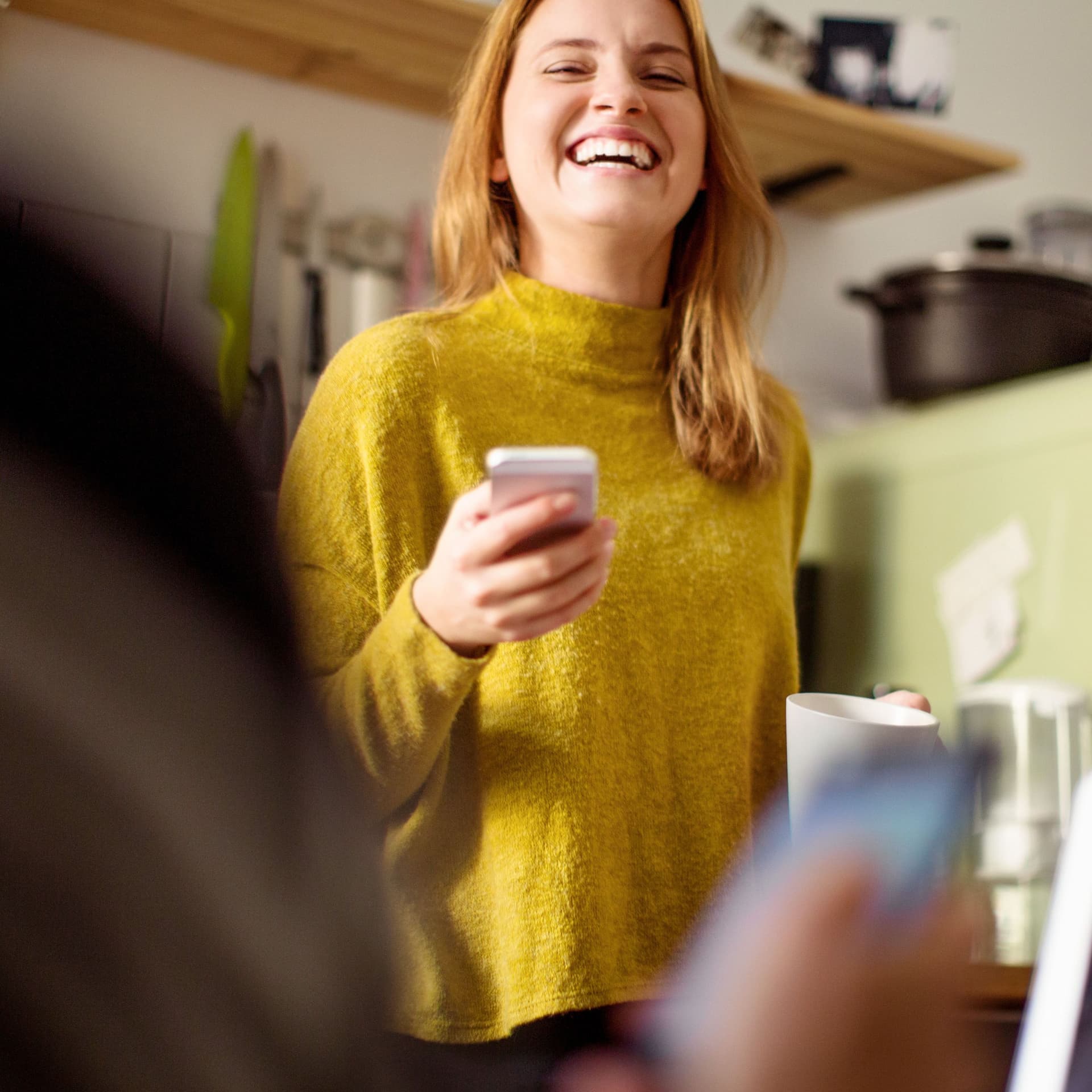 Lachende Frau mit Smartphone in der Hand in der  Küche.