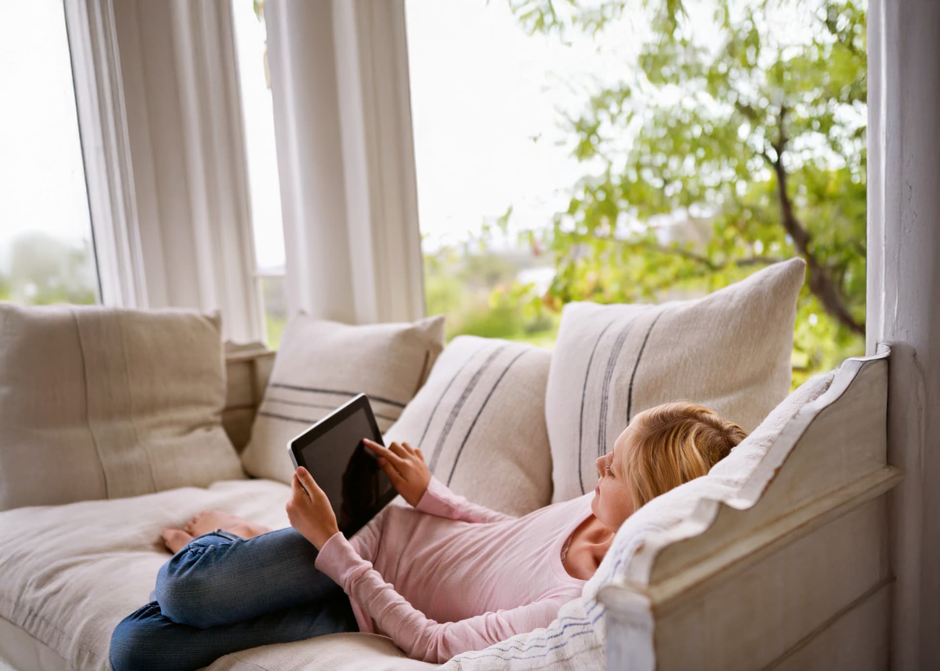 Eine Junge Frau liegt auf einem Sofa und benutzt ein Tablet