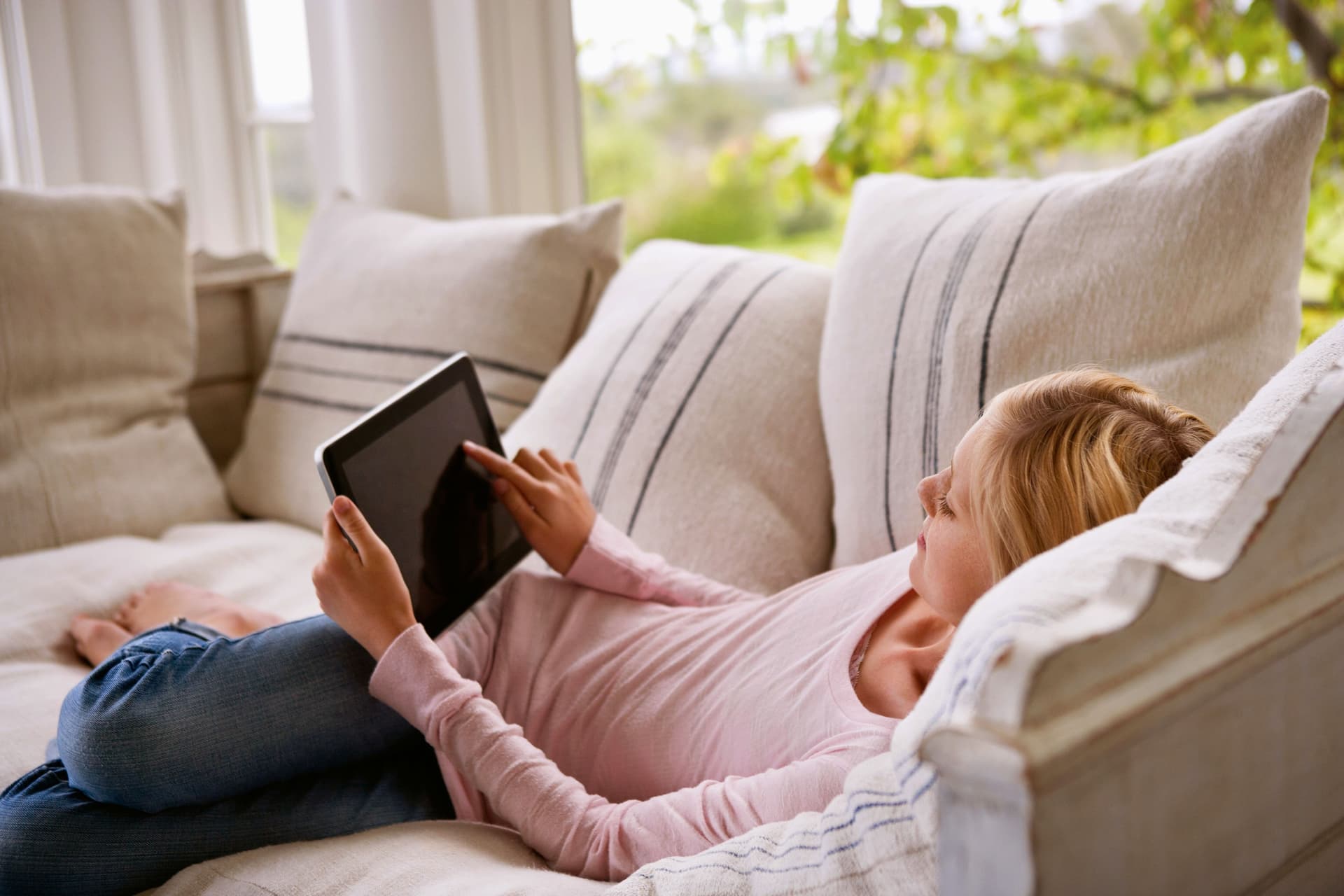 Eine Junge Frau liegt auf einem Sofa und benutzt ein Tablet