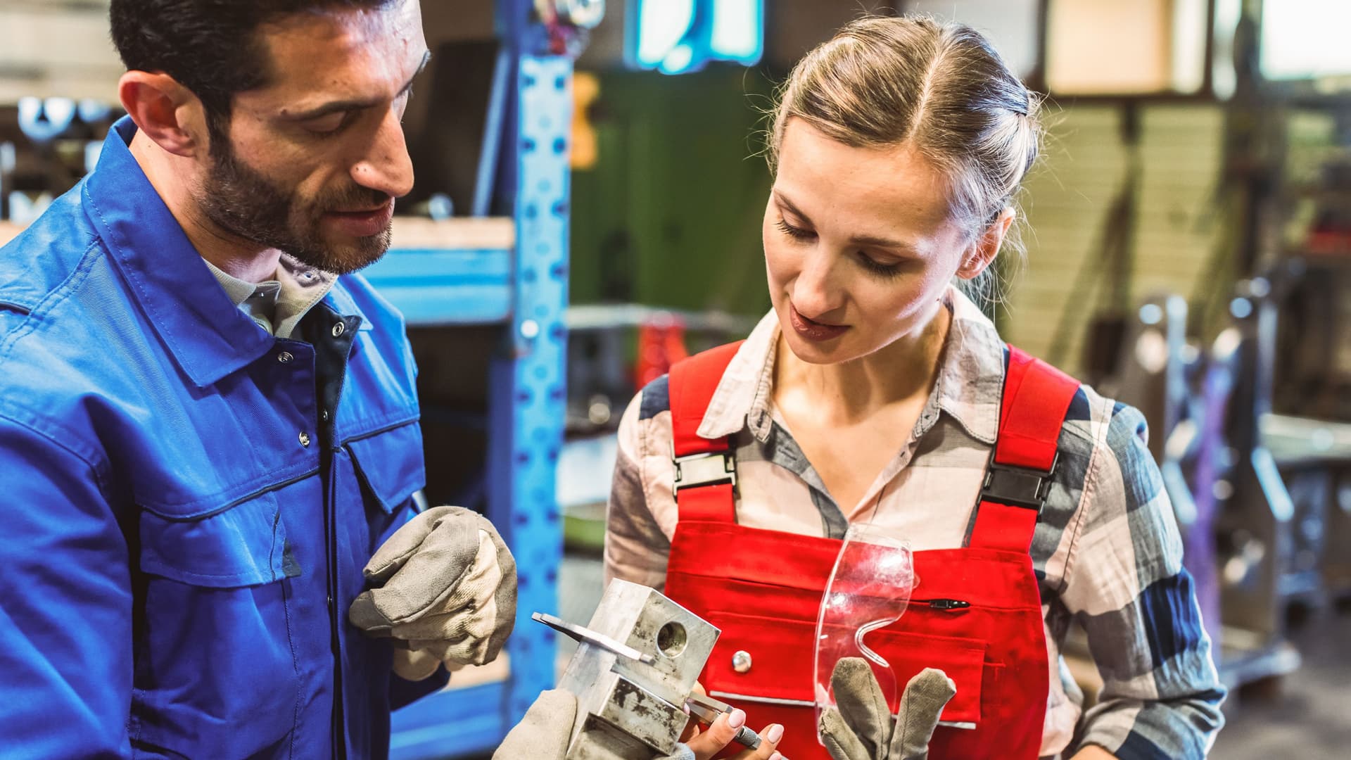 Arbeiterin und Arbeiter messen zusammen ein Metallwerkstück.