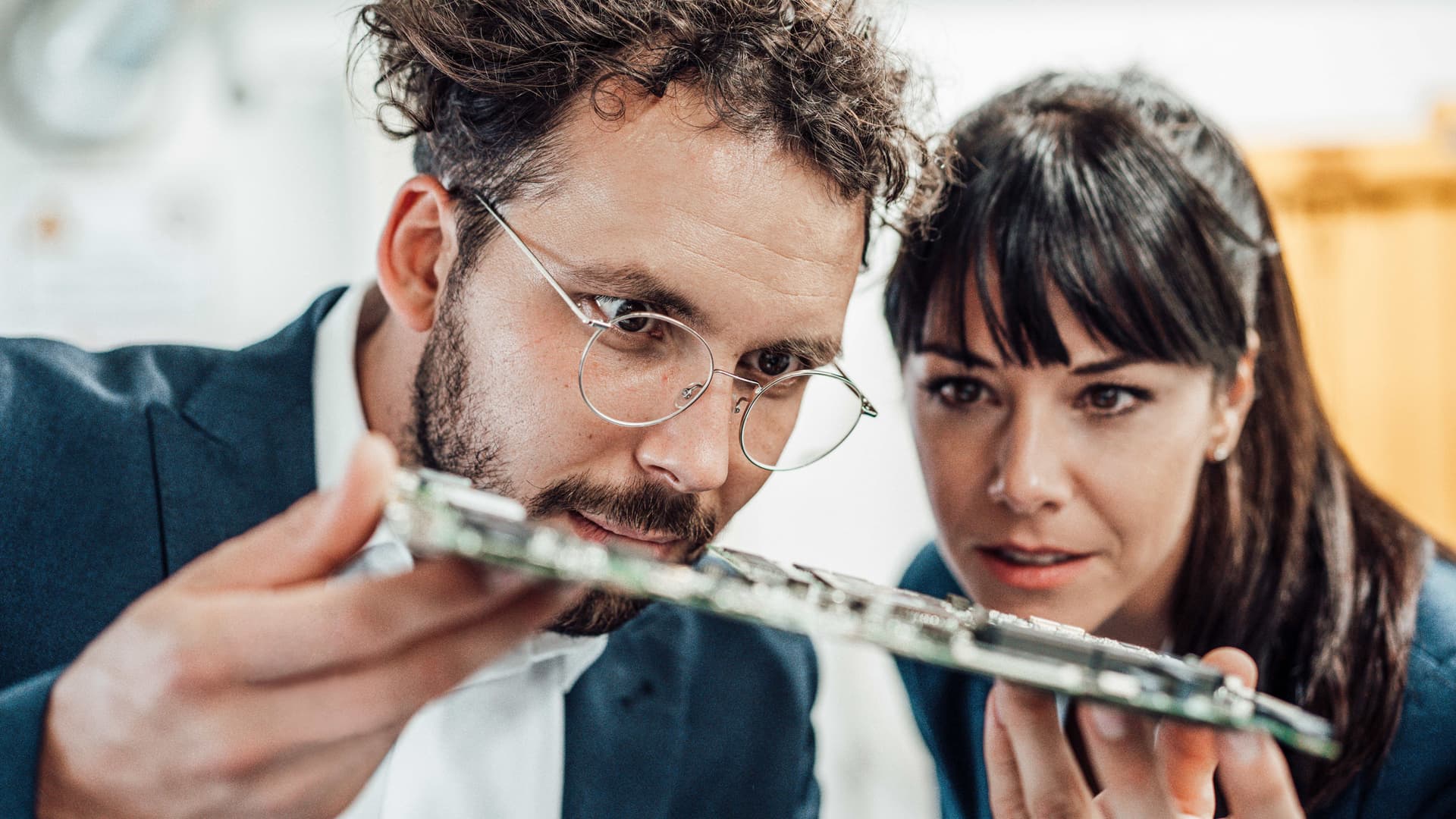 Ein Mann mit Brille und eine Frau untersuchen Leiterplatten in der Industrie.