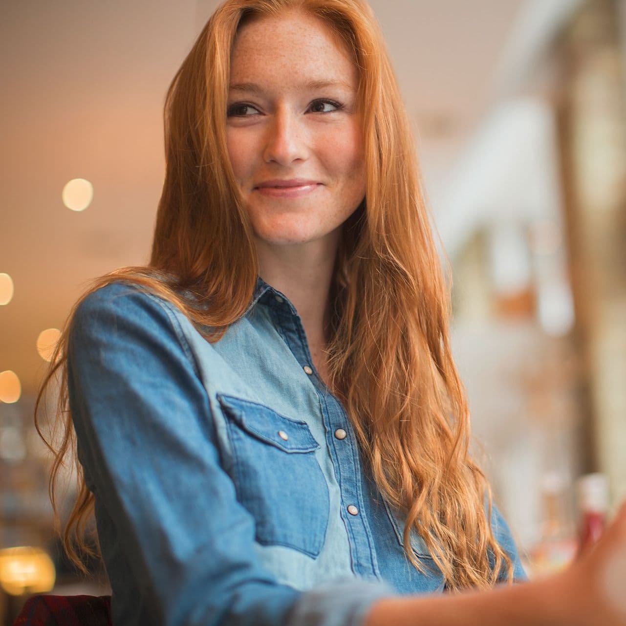 Eine junge Frau sitzt in einem Cafe und lächelt an der Kamera vorbei. Sie hat ein Tablet vor sich.