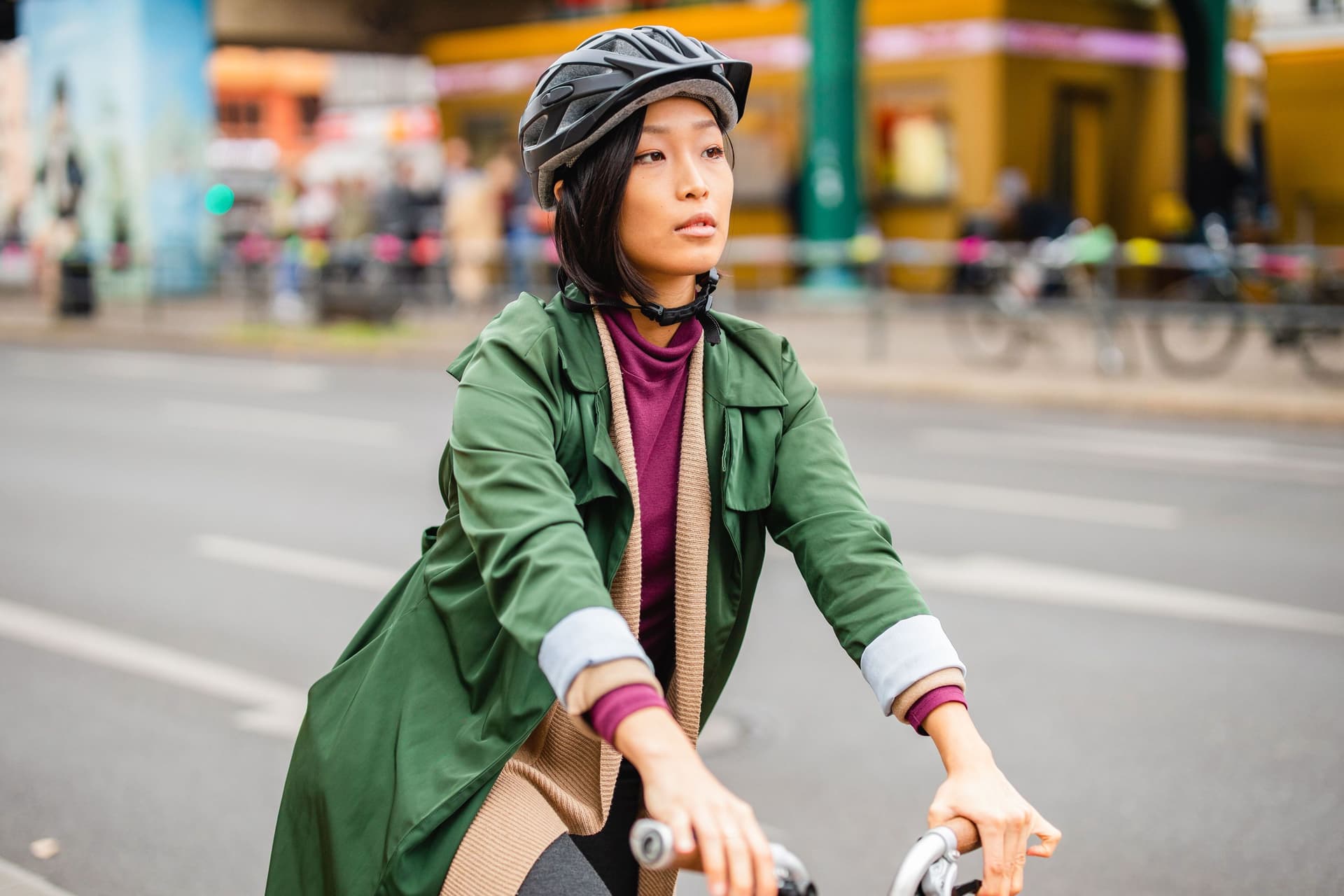 Eine Frau fährt in einer Großstadt Fahrrad. Sie trägt einen Fahrradhelm und elegante Kleidung.