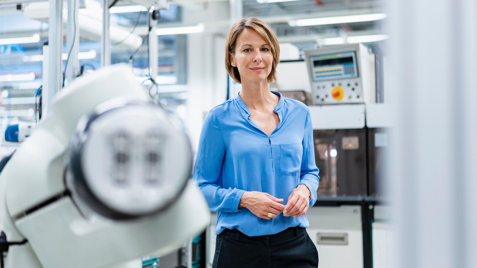 Porträt einer Frau am Montageroboter in einer Fabrik. Sie lächelt in die Kamera.