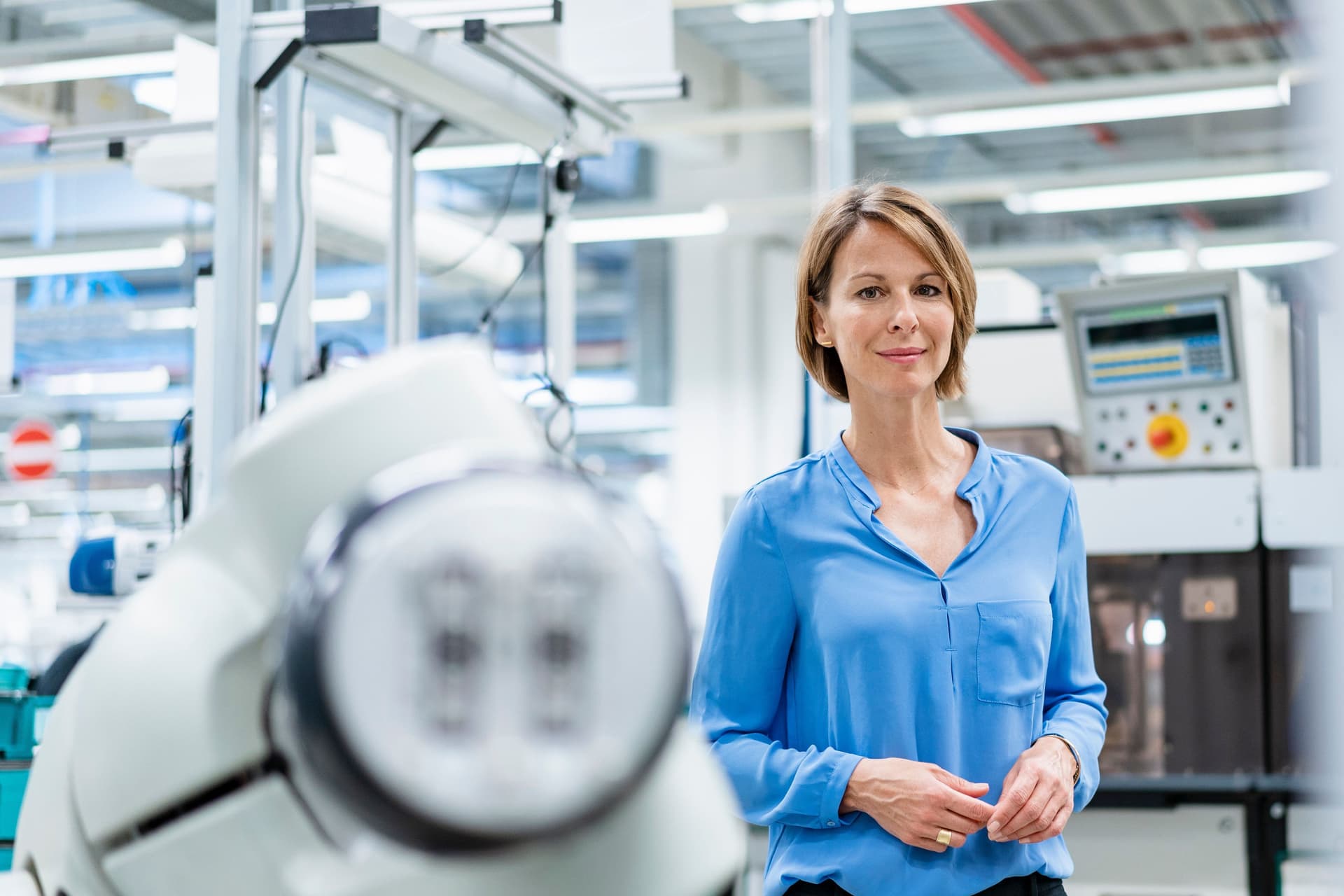 Porträt einer Frau am Montageroboter in einer Fabrik. Sie lächelt in die Kamera.