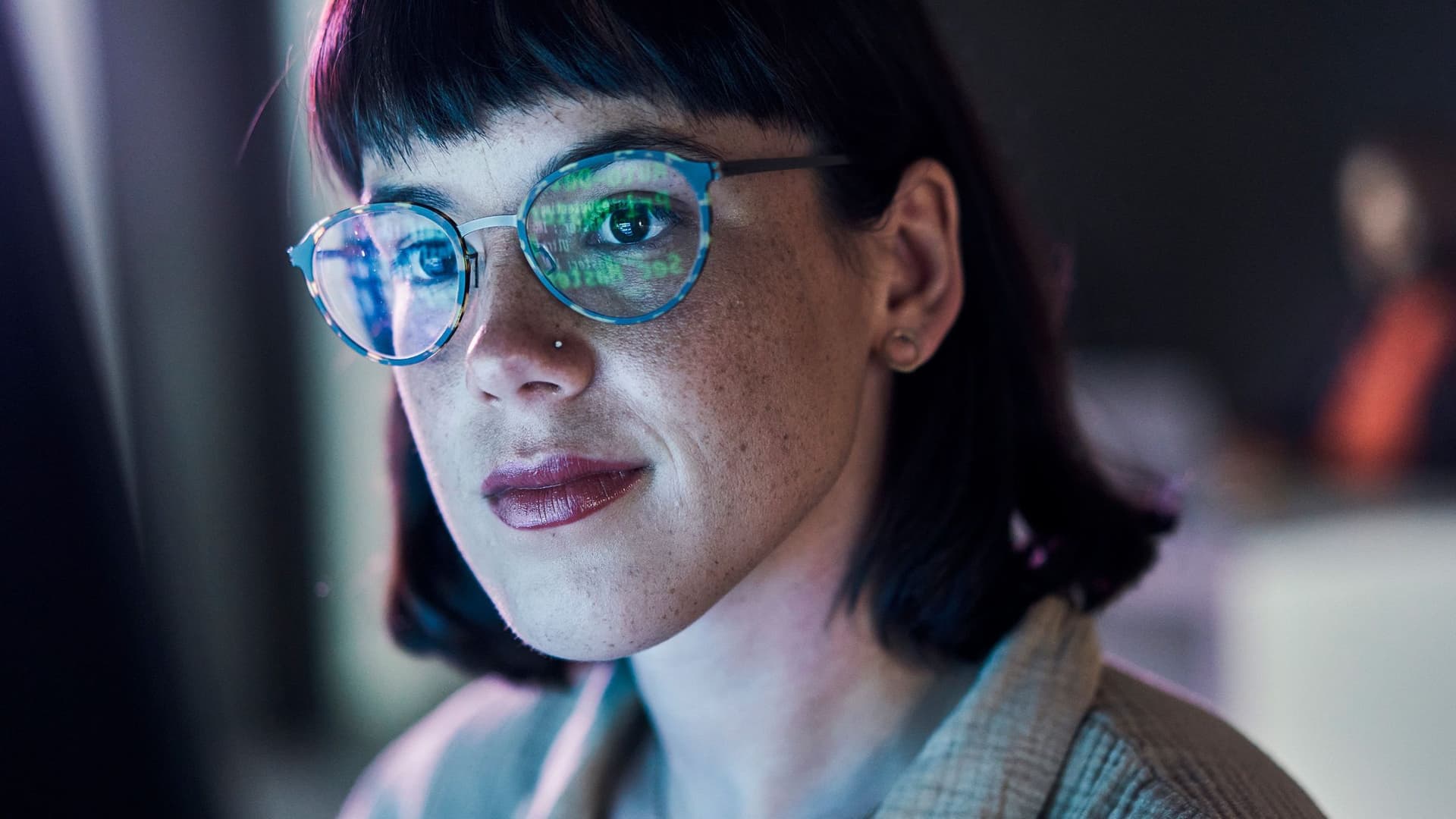 Ein Frau schaut lächelnd auf einen Monitor. Es spiegeln sich Zahlen auf ihrer Brille