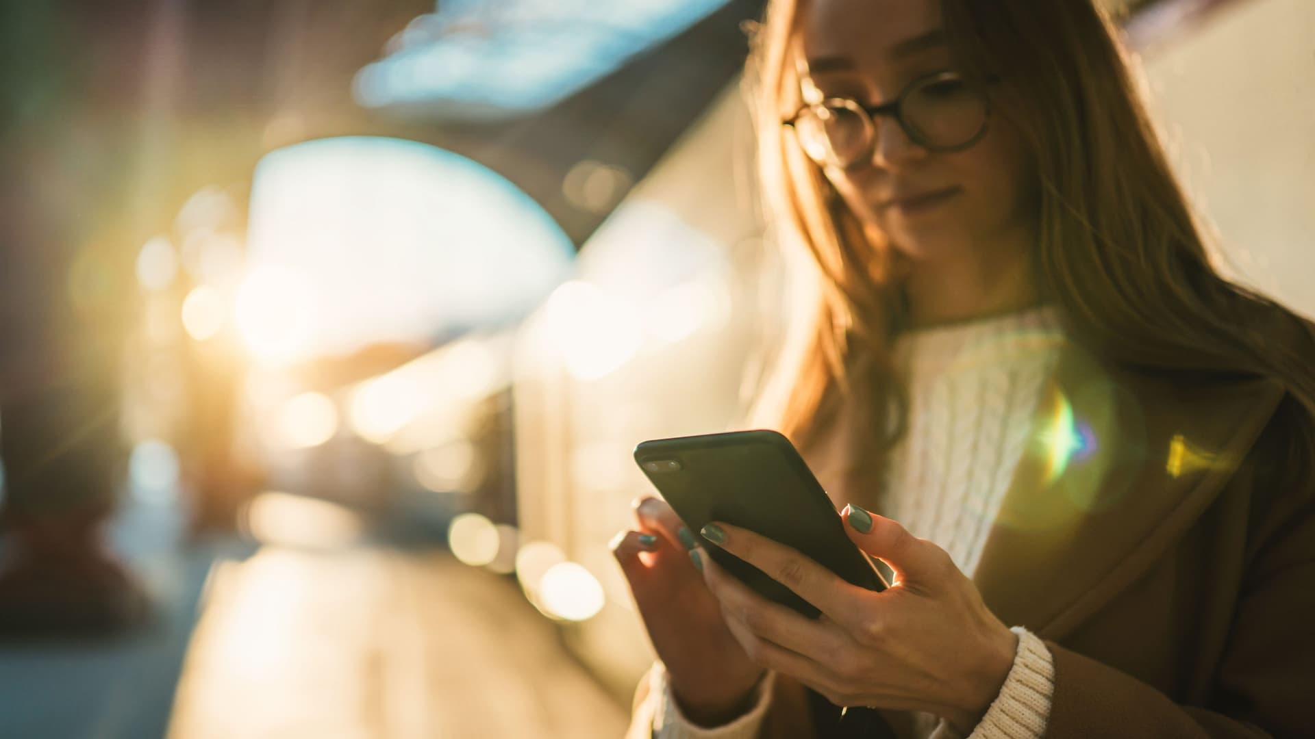 Junge Frau im Gegenlicht schaut auf Handy am Bahnhof.