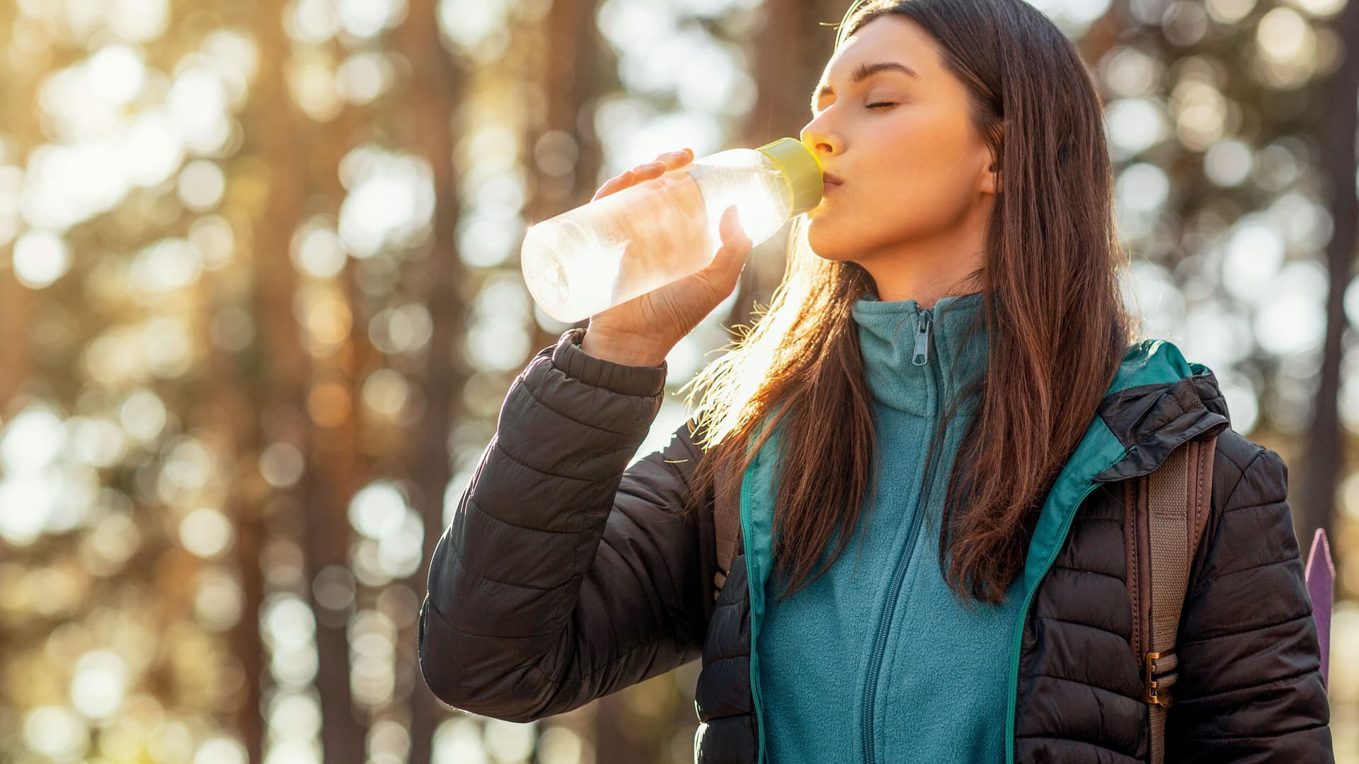 Junge Frau trinkt aus Wasserflasche im Wald.