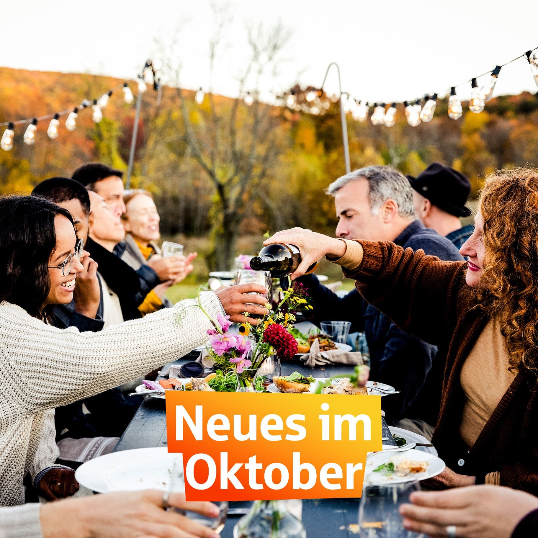 Freunde sitzen bei einem Dinner zusammen draussen. Darauf steht "Neues im Oktober"