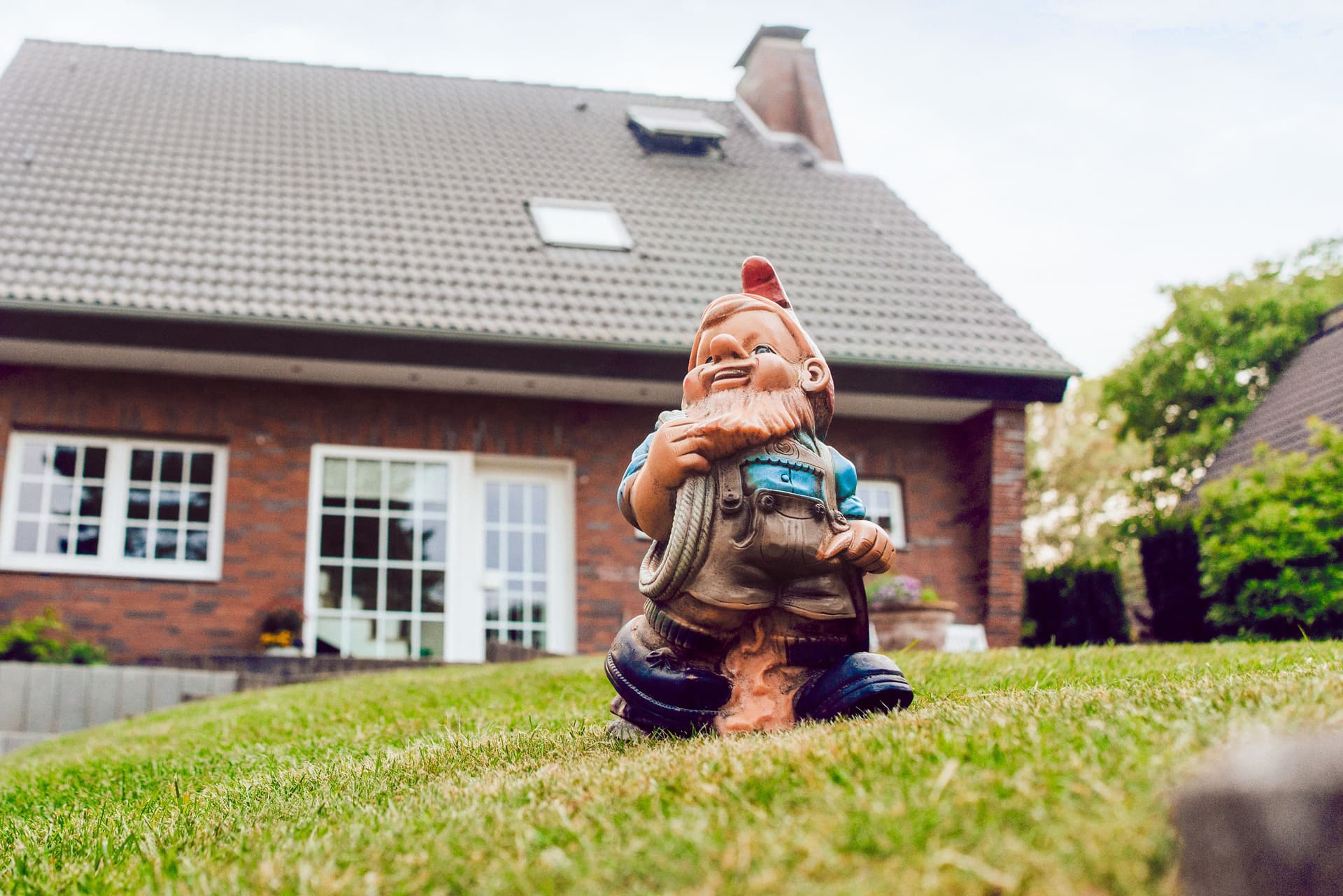 Aufnahme eines Gartenzwergs, der auf einer grünen Wiese vor einem Einfamilienhaus steht.