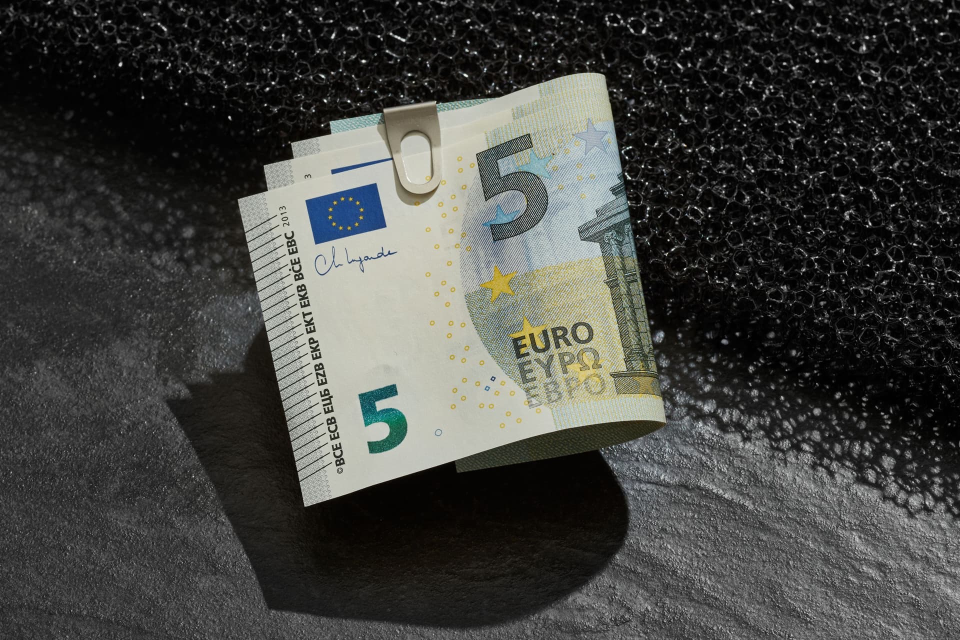 Ein Buendel 5-Euroscheine mit einer klammer befestigt liegt auf einer Kante.