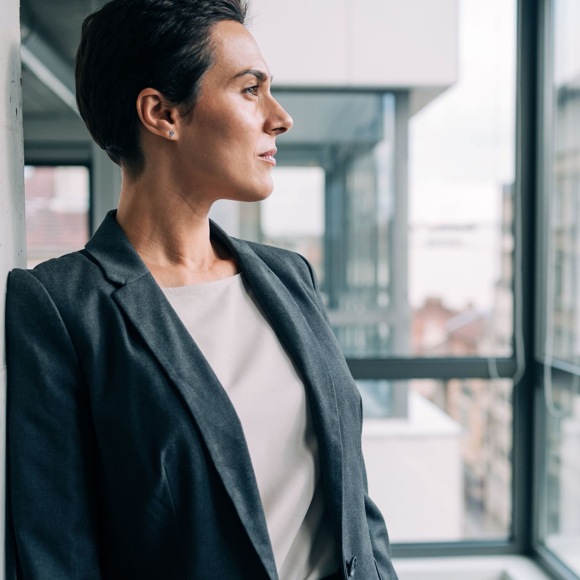 Eine Frau in Business Kleidung blickt aus dem Fenster eines Bürohochhauses.