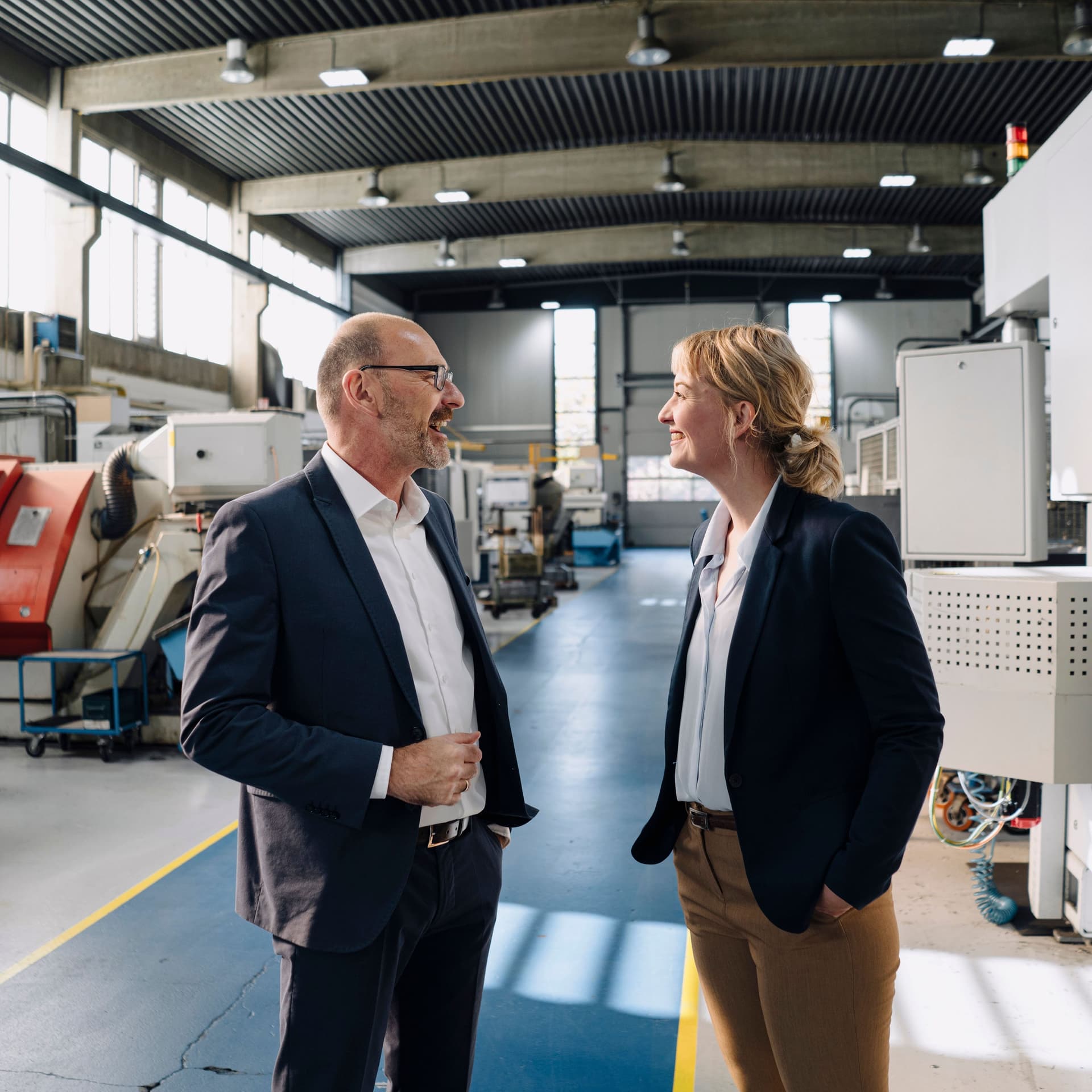 Geschäftsmann und Geschäftsfrau unterhalten sich in einer Fabrik und lachen dabei.