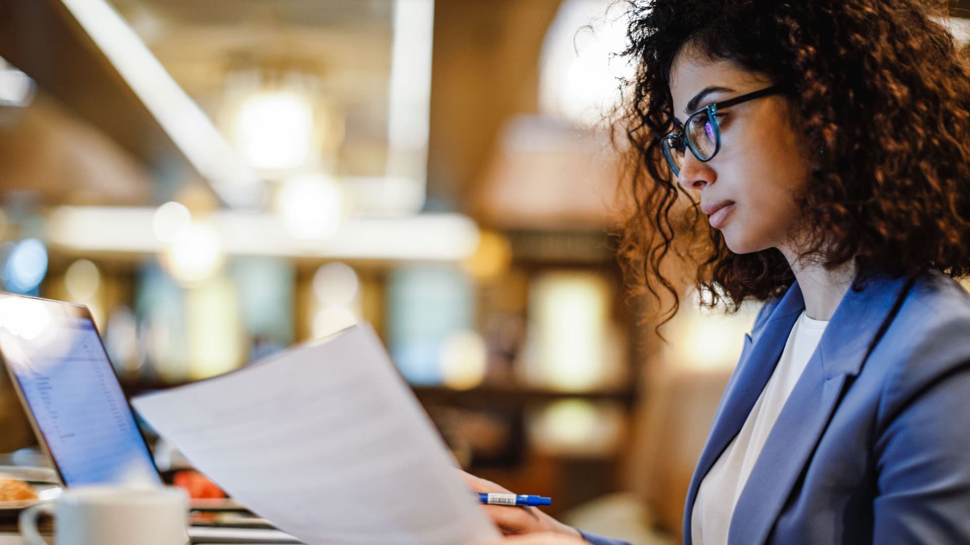 Eine Frau in Business-Kleidung sitzt in einem Café und arbeitet mit ihrem Laptop.