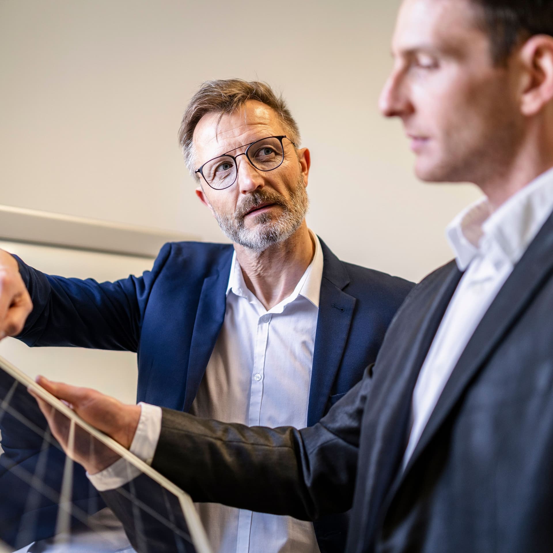 Zwei Geschäftsmänner im Büro diskutieren. Sie haben eine Solarzelle vor sich.