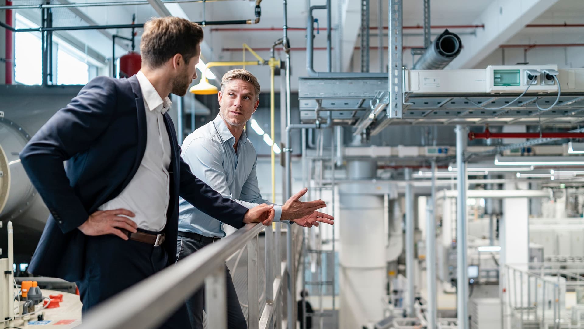 Zwei Männer in Business-Kleidung unterhalten sich in einer modernen Fabrik.