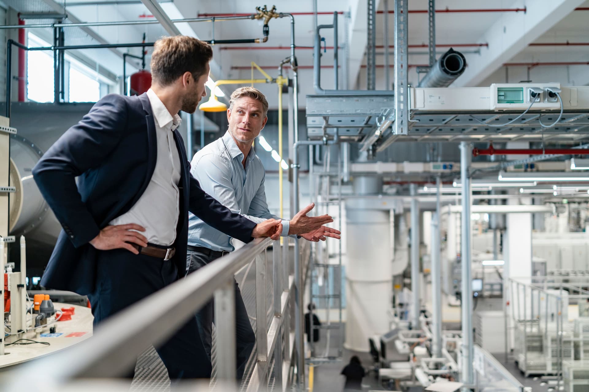 Zwei Männer in Business-Kleidung unterhalten sich in einer modernen Fabrik.