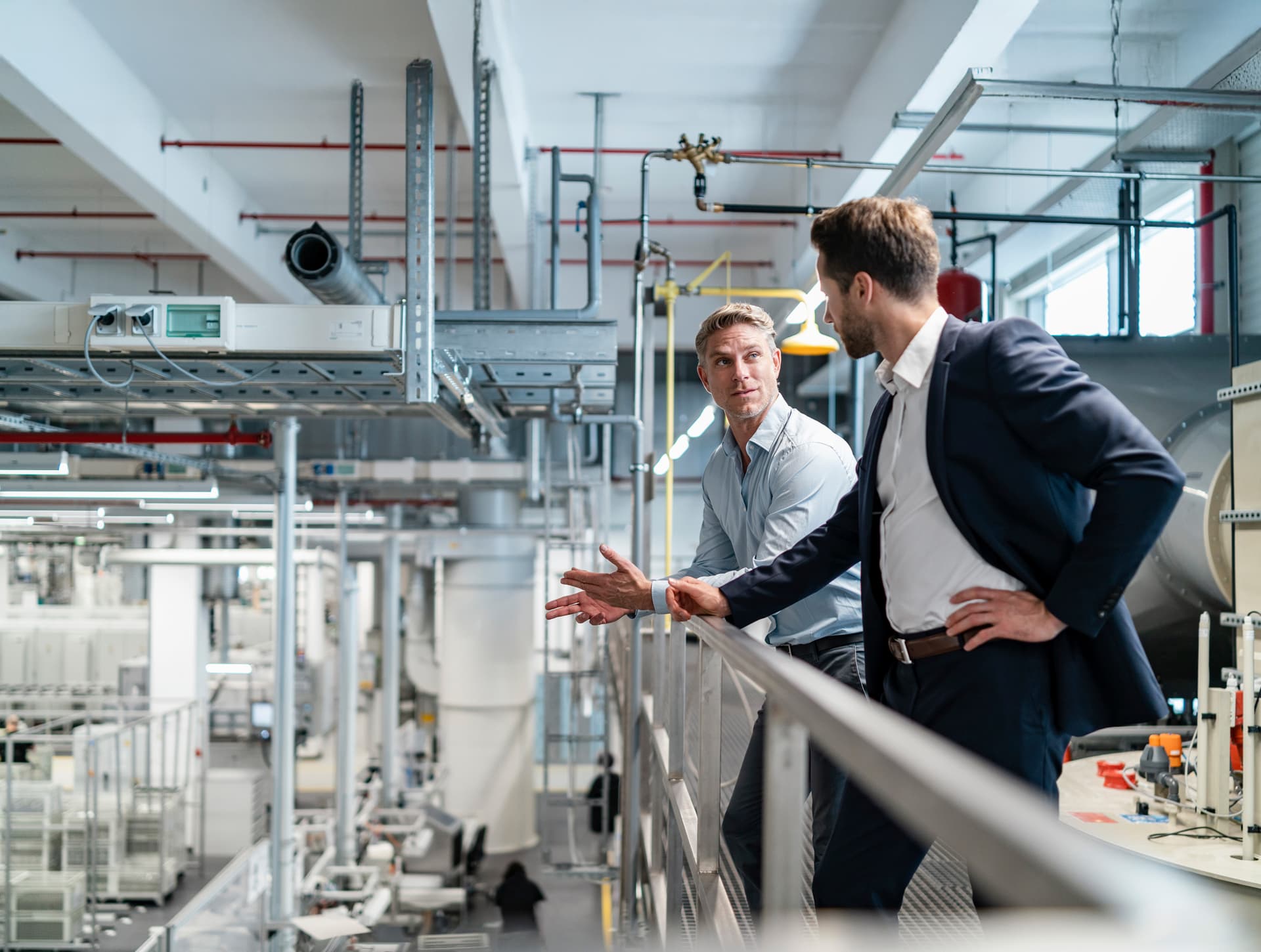 Zwei Männer in Business-Kleidung unterhalten sich in einer modernen Fabrik.