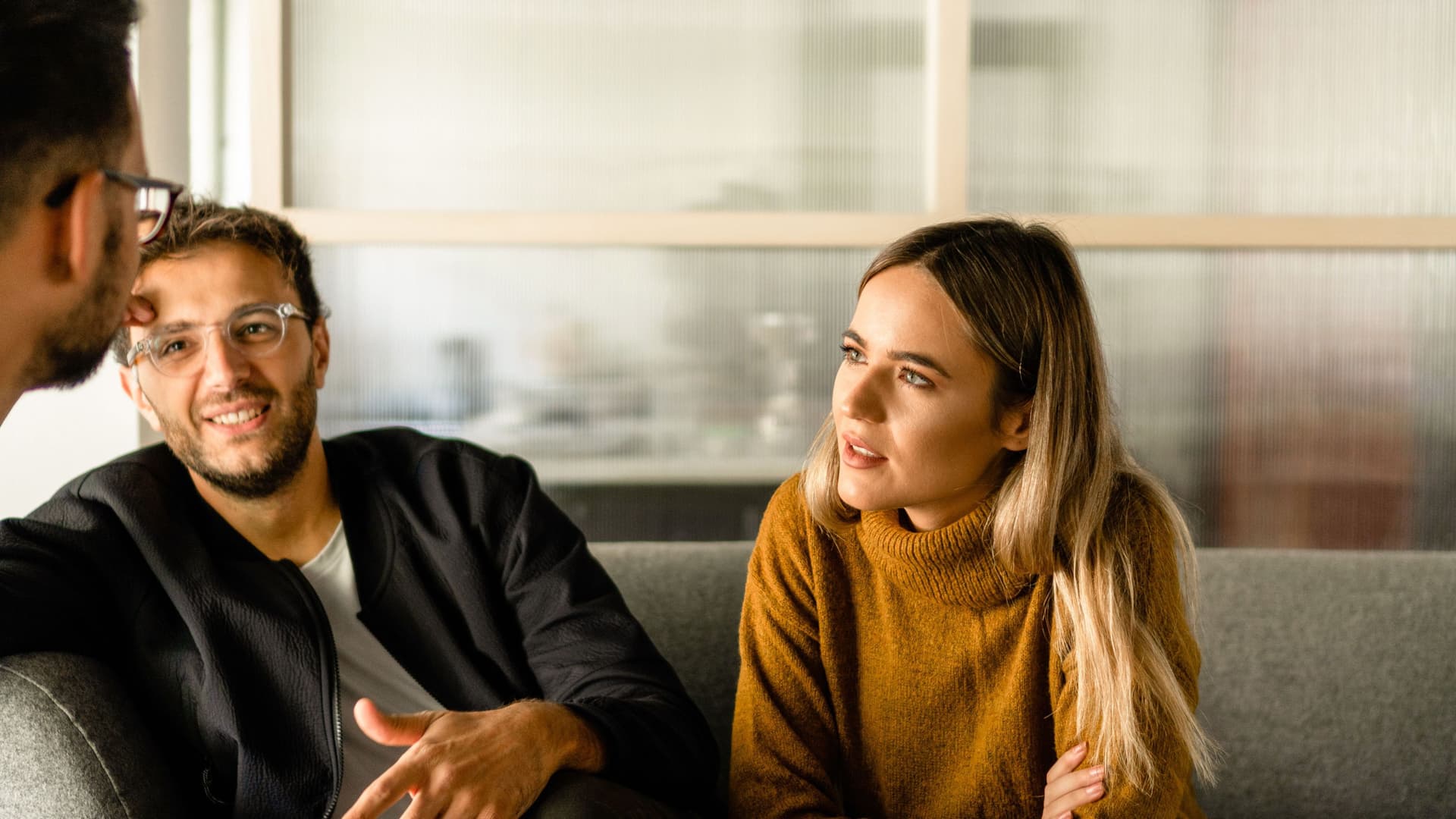 Zwei Männer und eine Frau sitzen zusammen in einem Meeting im Büro.