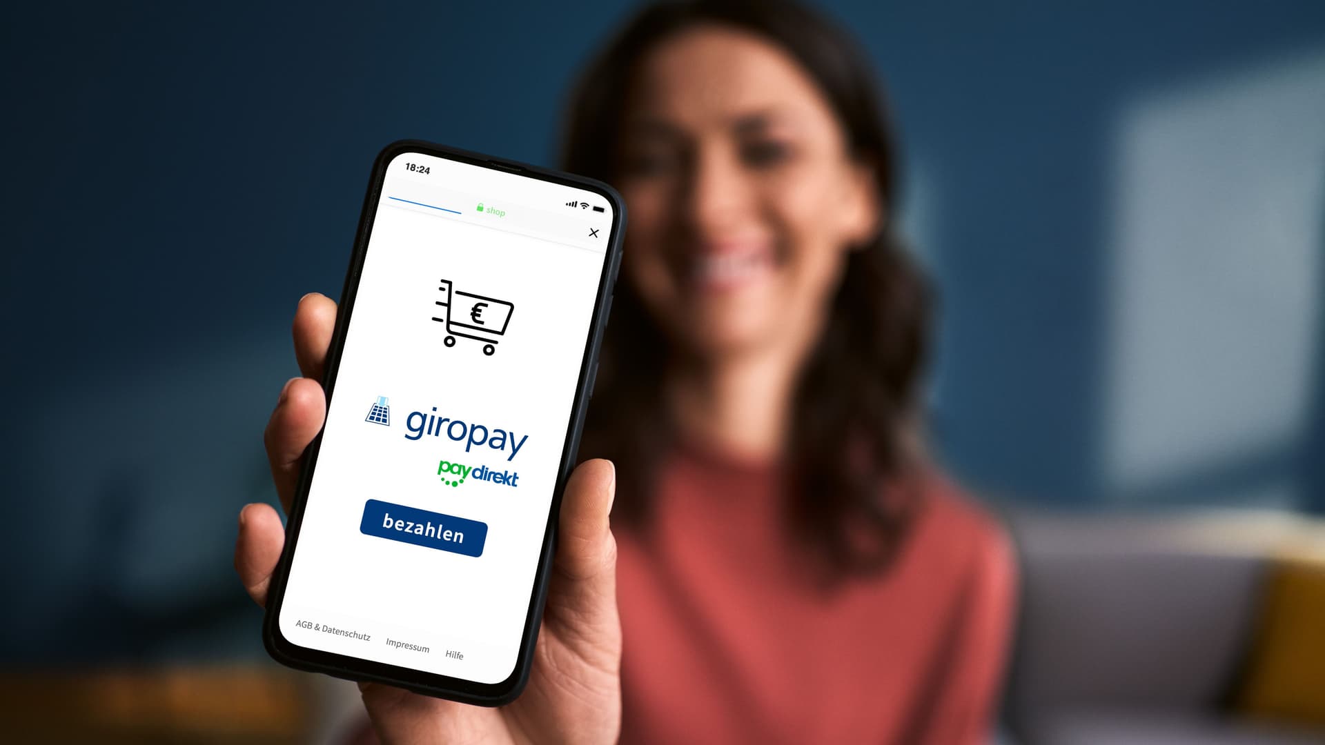 Frau, auf einen Sofa sitzend, hält Handy mit Giropay App vor die Kamera