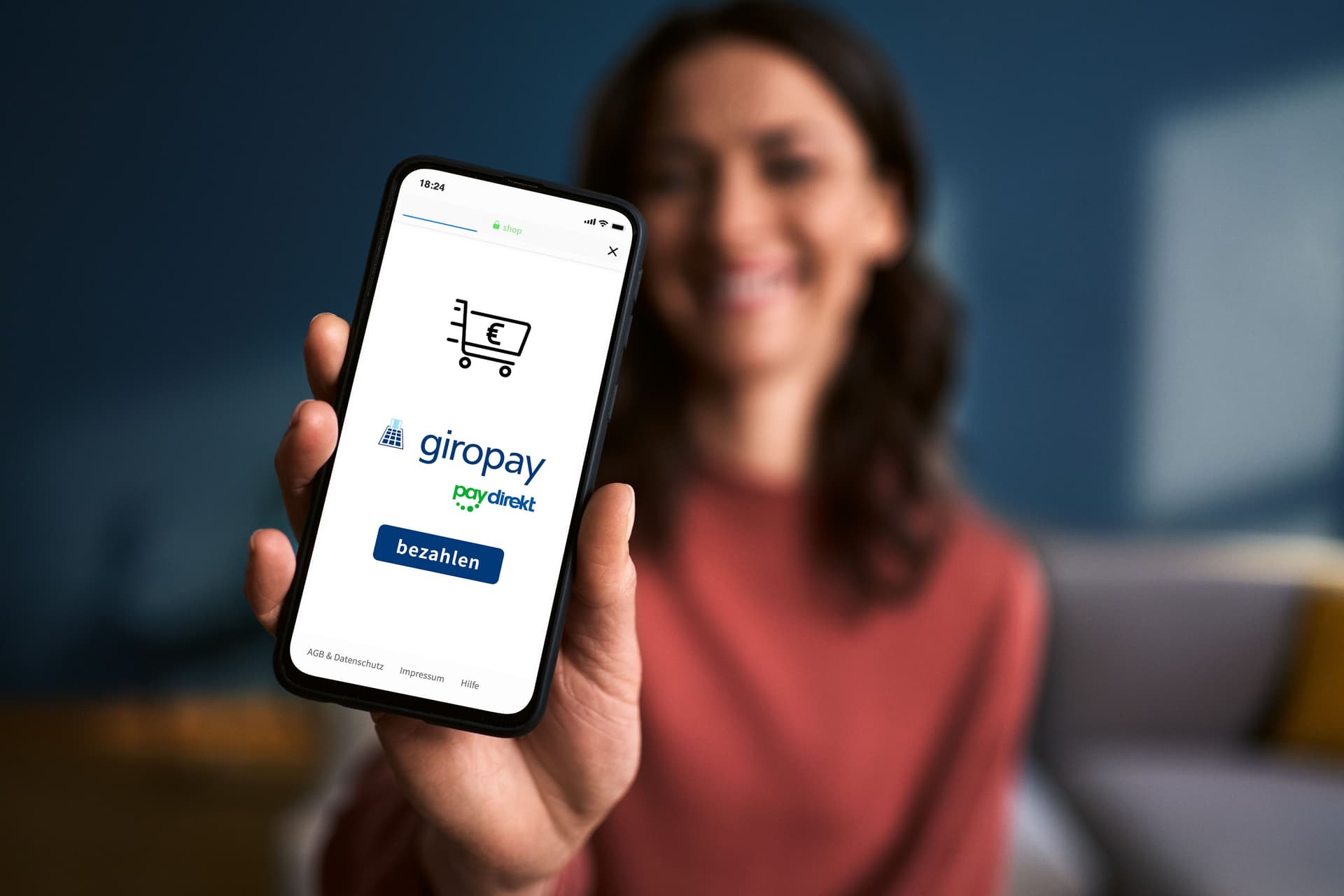 Frau, auf einen Sofa sitzend, hält Handy mit Giropay App vor die Kamera
