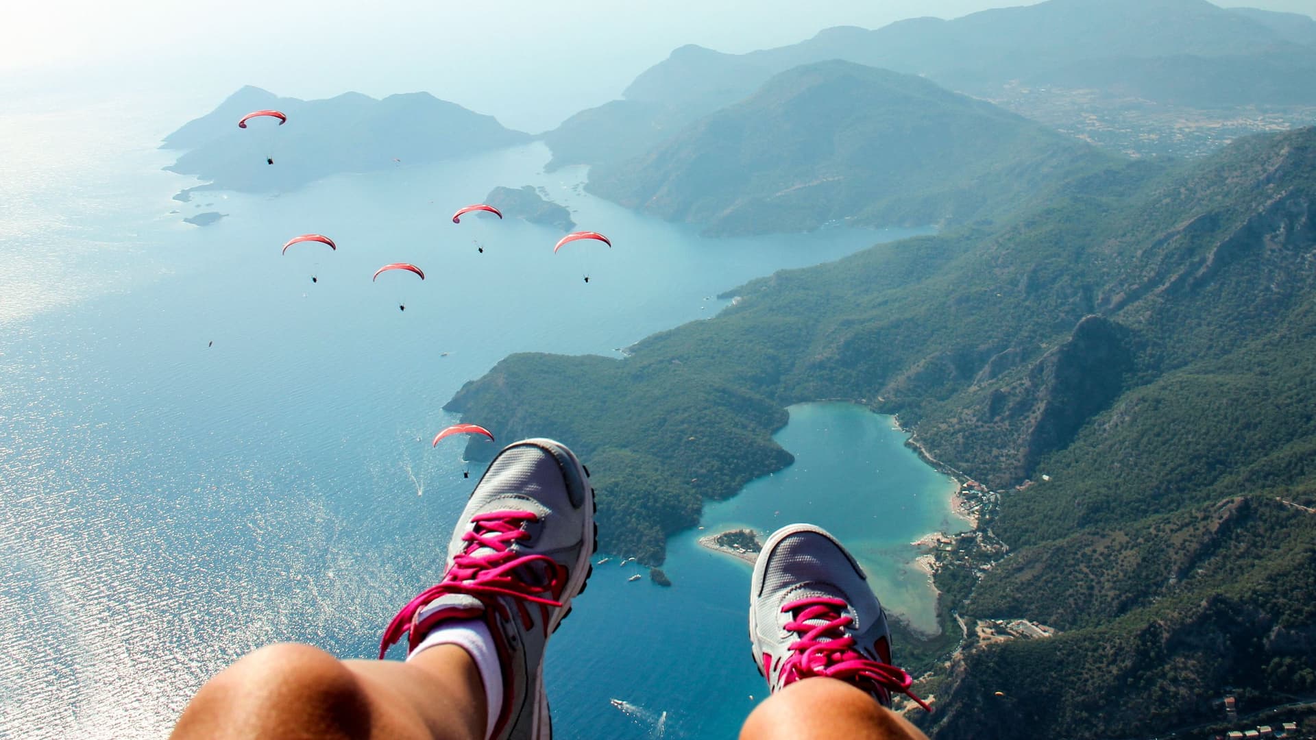 Paraglider fliegen über einer Küstenlandschaft bei sonnigem Wetter.