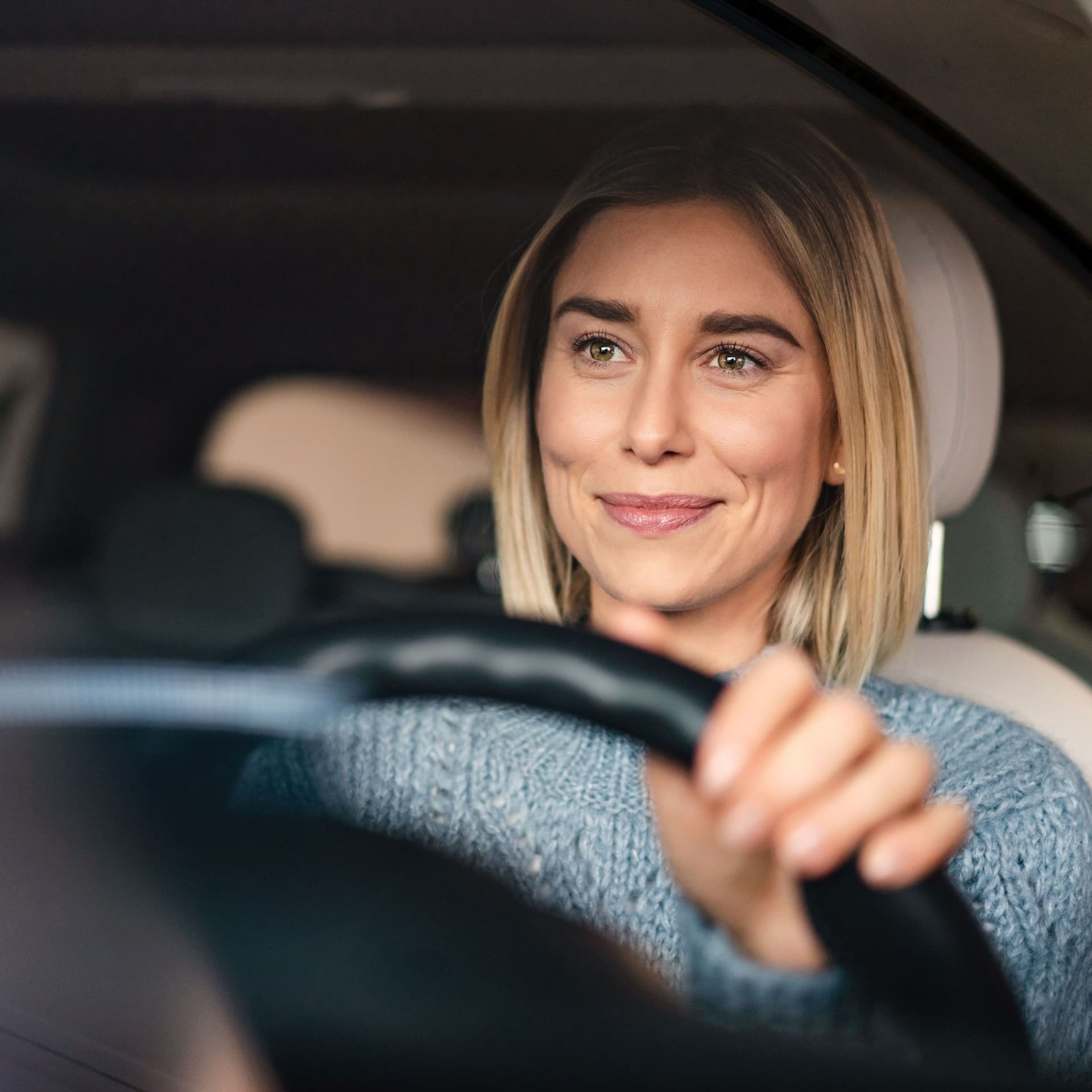 Porträt einer lächelnden Frau hinter dem Steuer ihres Autos.