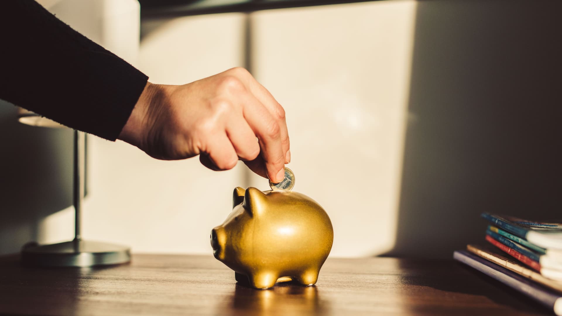 Woman putting coin into a golden piggy bank.