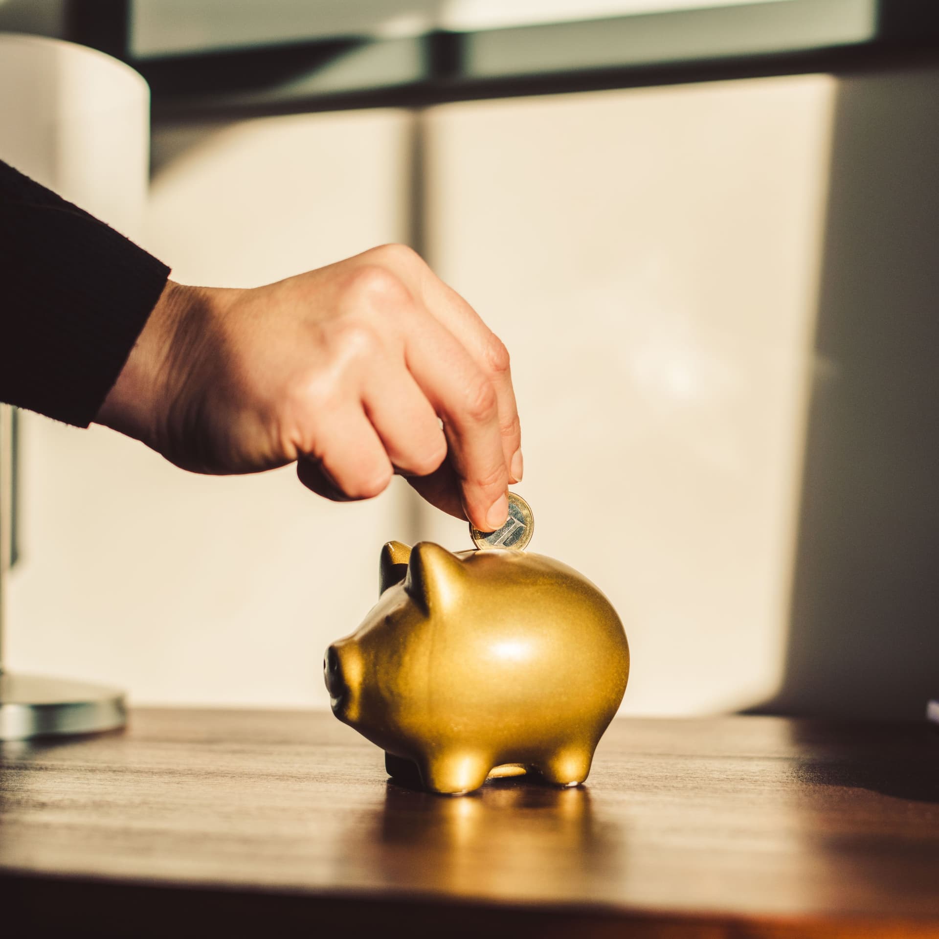 Woman putting coin into a golden piggy bank.