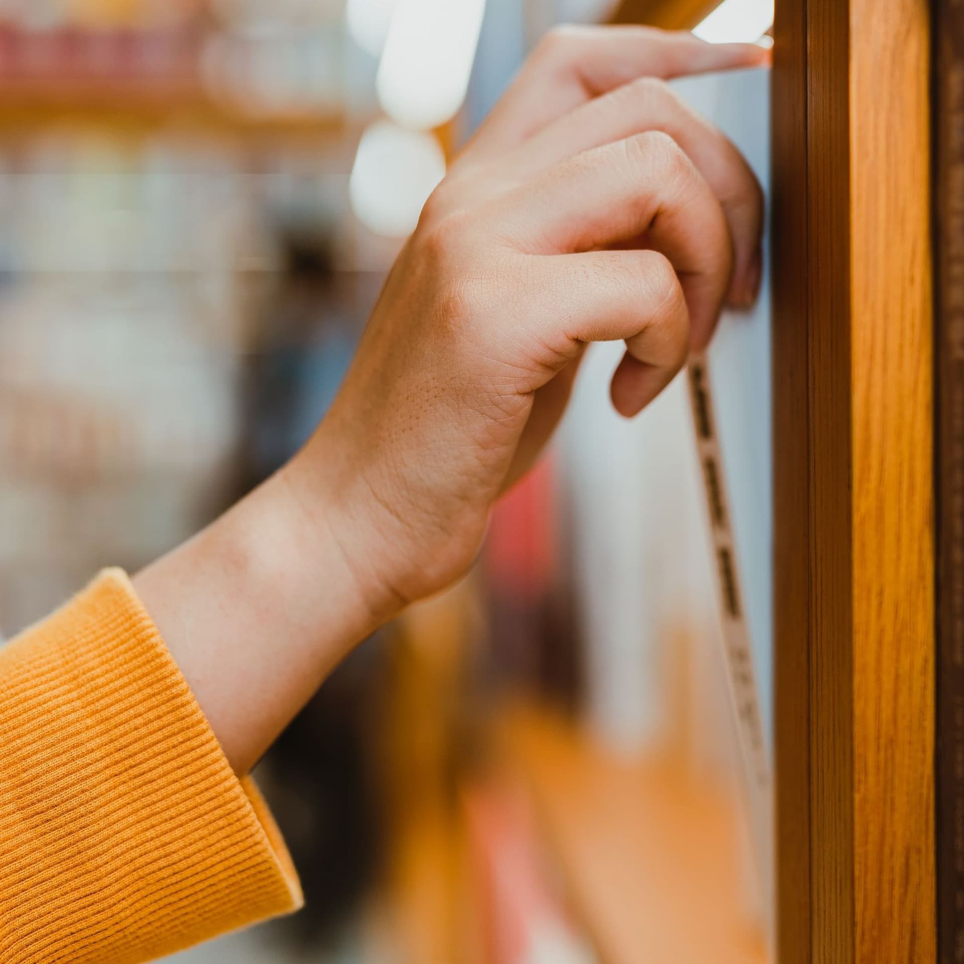 Seitliche Nahaufnahme von einem Arm mit orange farbenen Pullover. Die Hand zieht ein Buch aus einem Bücherregal.
