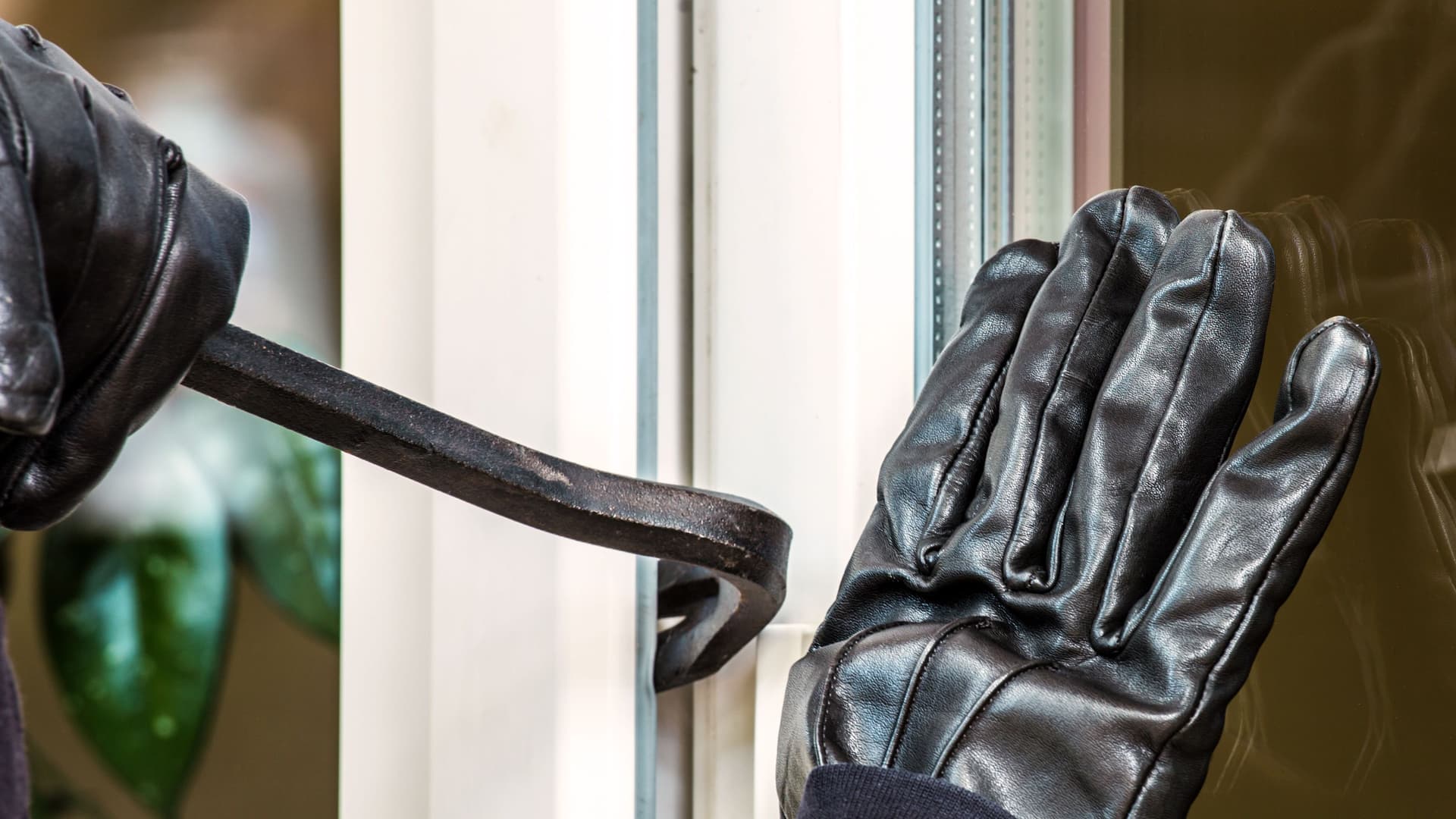 Nahaufnahme zweier Hände in schwarzen Handschuhen die versuchen mit Hilfe eines Brecheisens ein Tür aufhebeln.