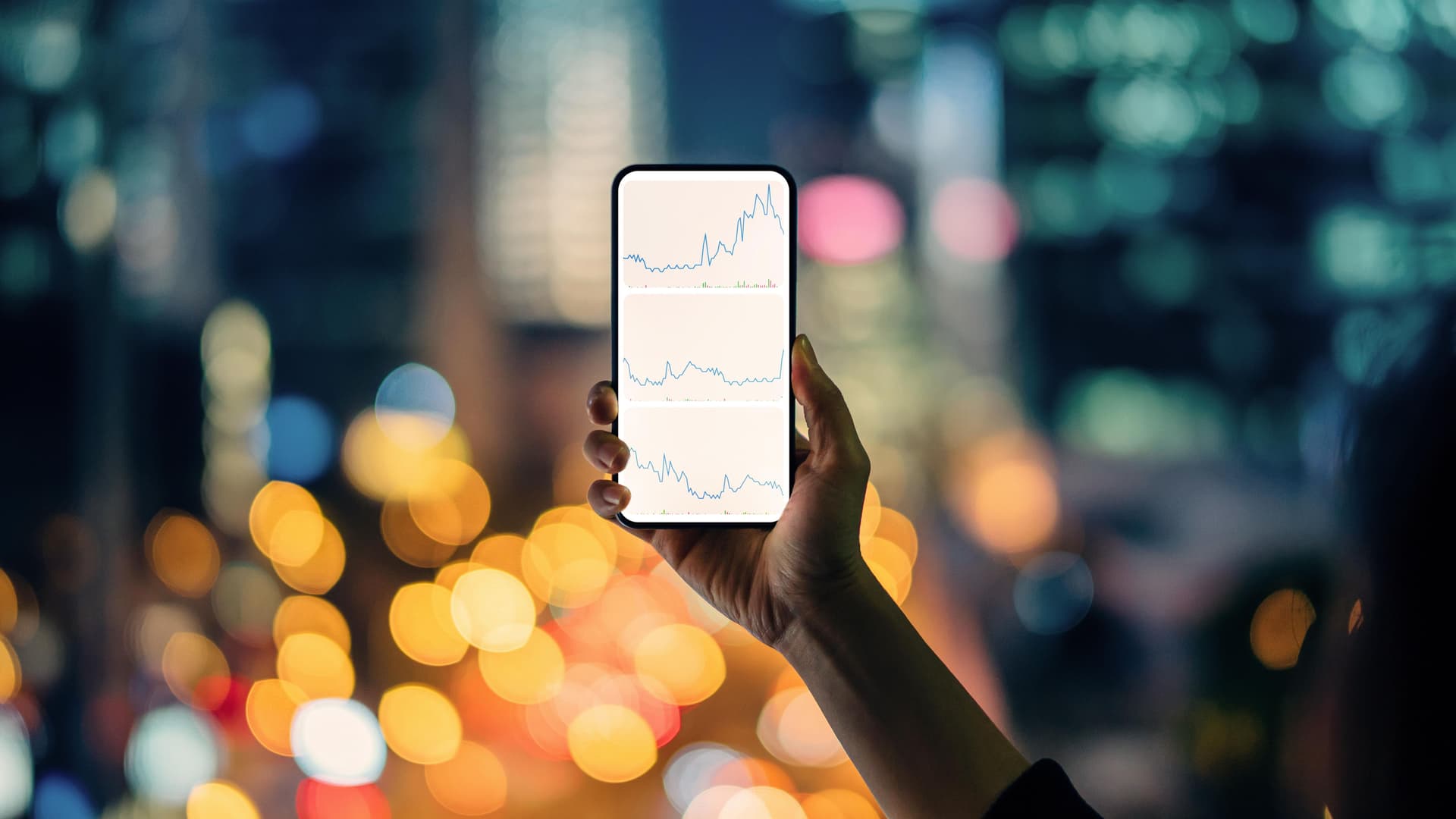 Person hält ein Smartphone mit Datenkurven auf dem Display in der Hand. 