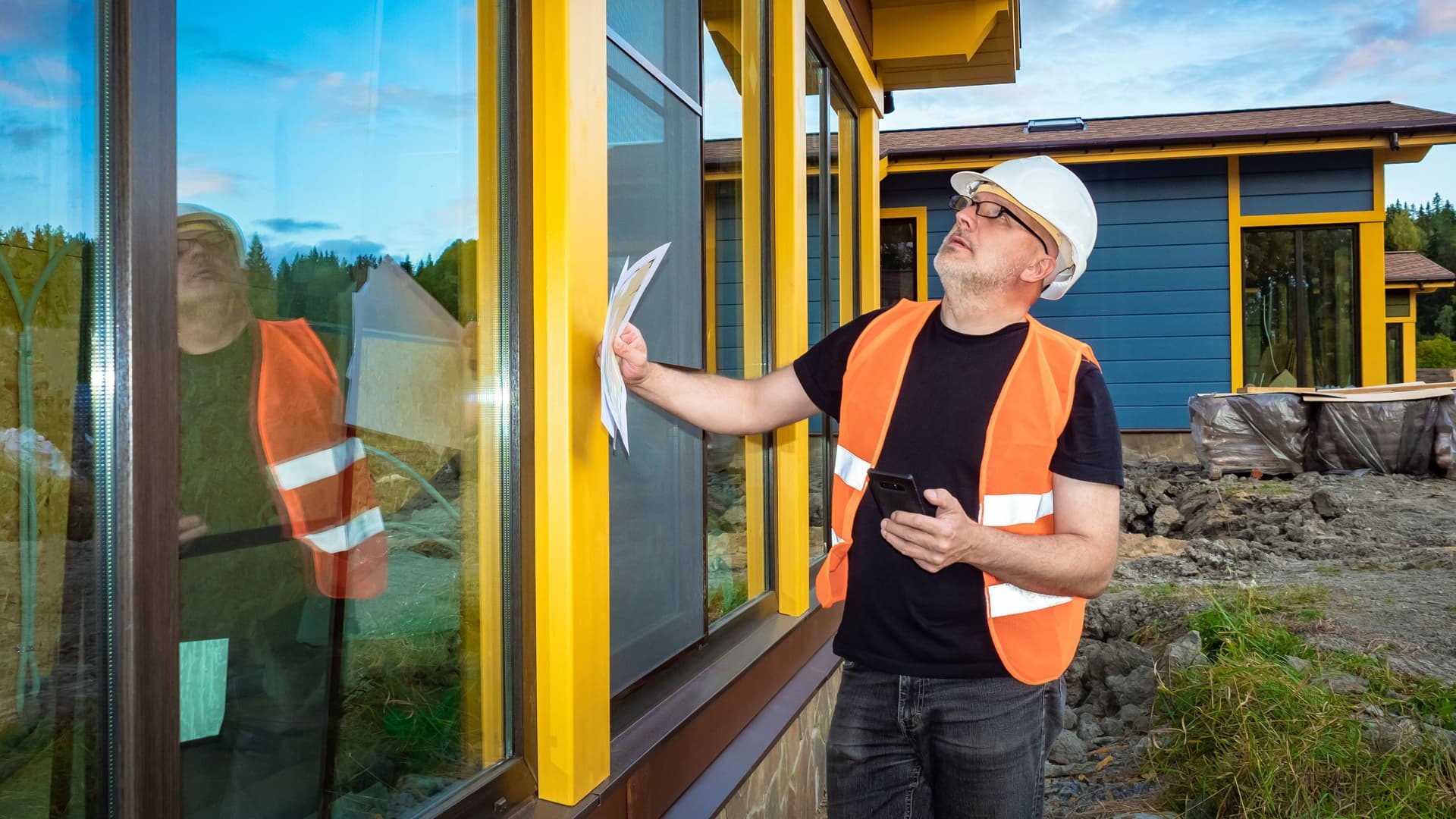 Ingenieur mit Warnweste und Helm prüft die Qualität der modernen Fensterfront.
