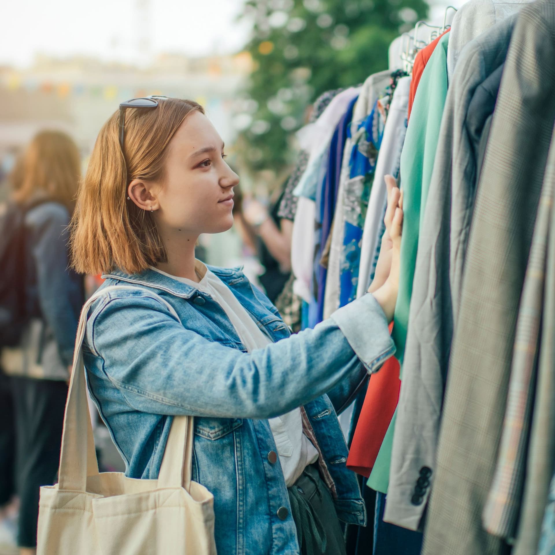 Junge Frau schaut auf einem Flohmarkt nach Jacken auf einem Garderobenständer